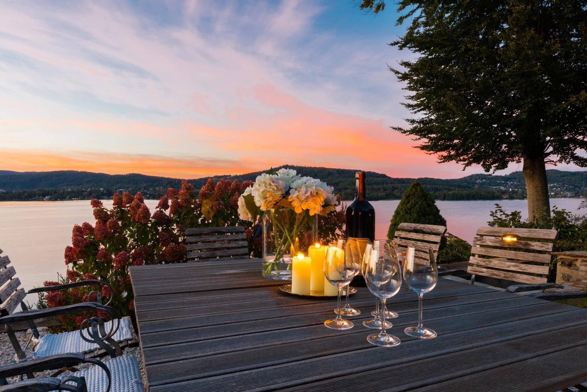 Romantischer Abend auf der Terrasse mit gedecktem Tisch, Kerzen und Seeblick bei Sonnenuntergang.