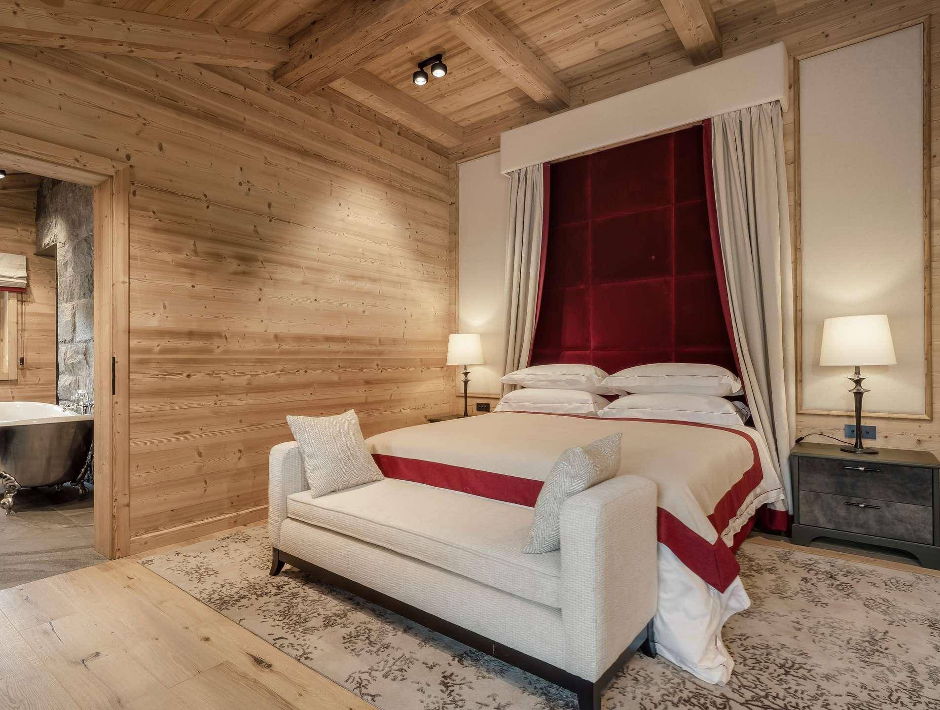 Elegantes Schlafzimmer mit Holzwänden, rotem Samt-Kopfteil und Zugang zu einem luxuriösen Bad mit freistehender Wanne.