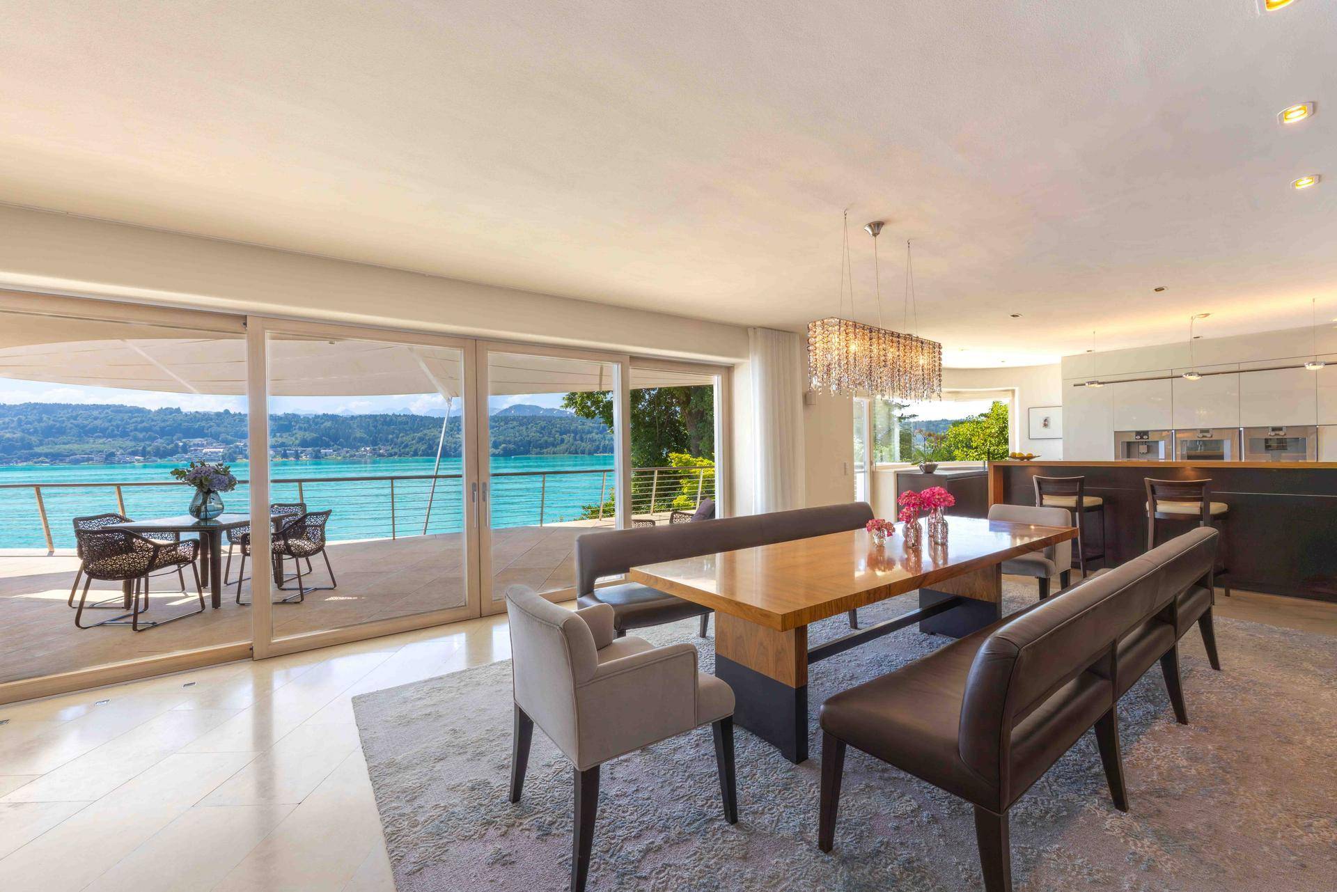 Eleganter Essbereich mit Holztisch, Sitzbänken und Panoramablick auf den See von der angrenzenden Terrasse.