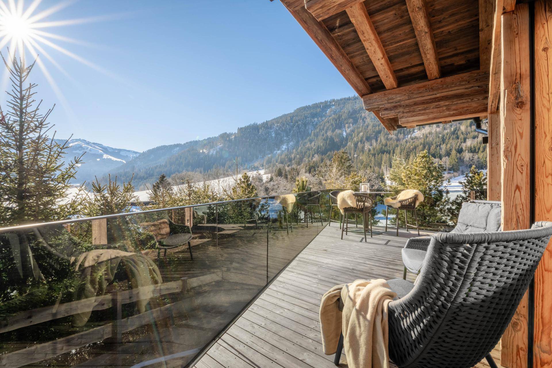 Sonnige Holzterrasse mit Glasgeländer und atemberaubendem Bergblick, ideal zum Entspannen im Freien.