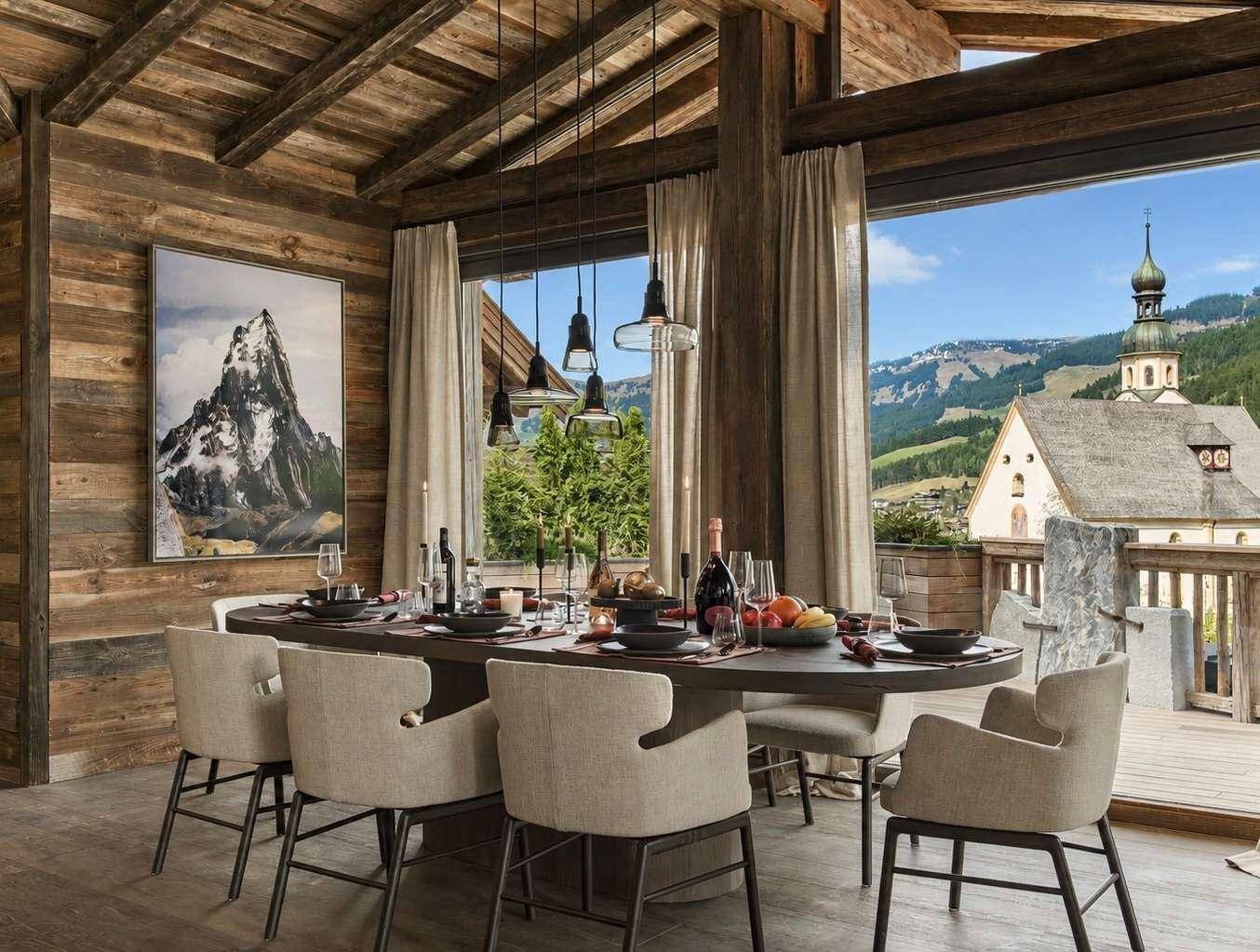 Eleganter Essbereich mit Holzwänden, großem Esstisch und Panoramablick auf die Berge und ein Dorf.