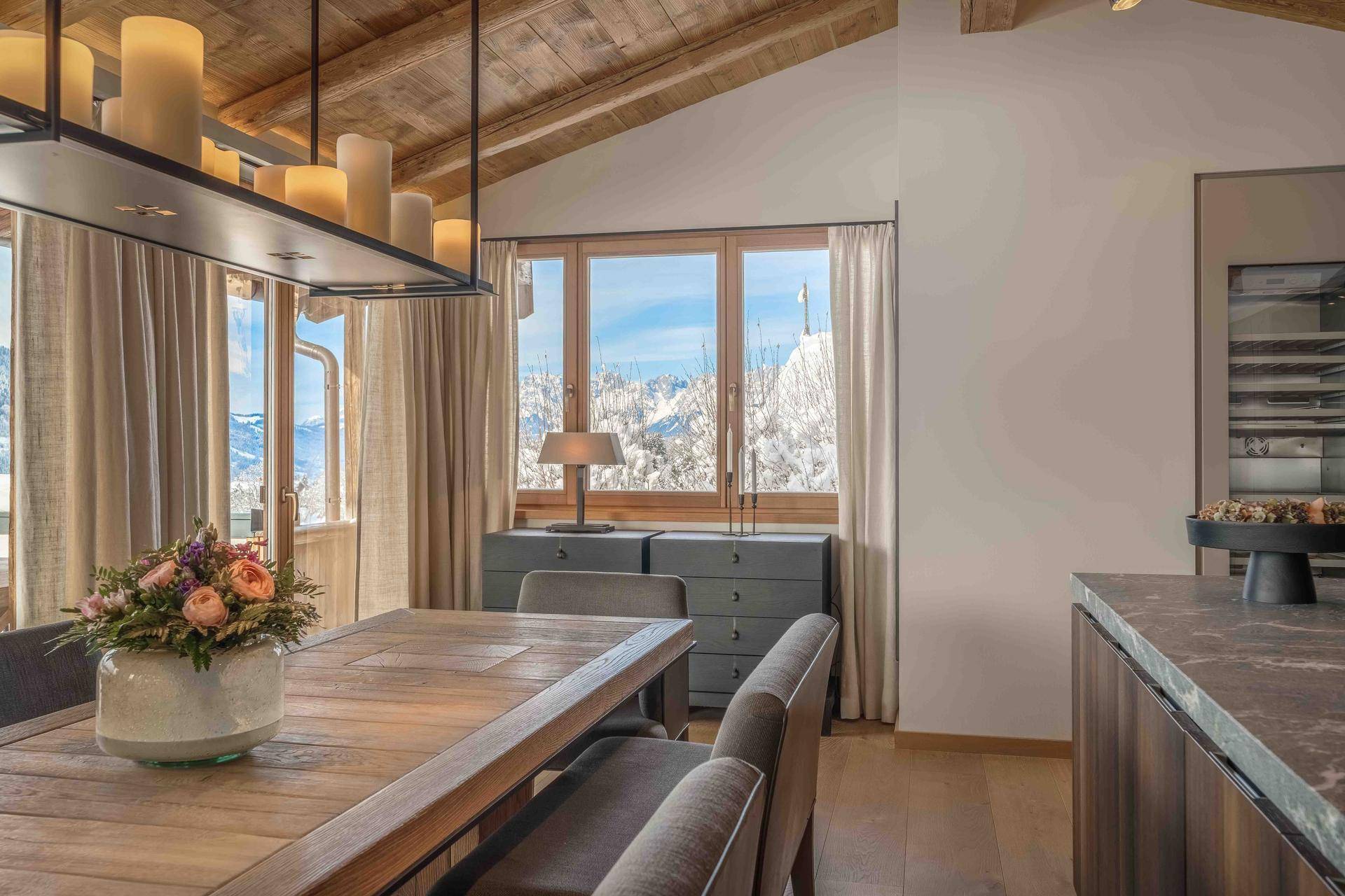 Eleganter Essbereich mit Holztisch, Kerzenleuchter und Fensterblick auf die winterliche Berglandschaft.