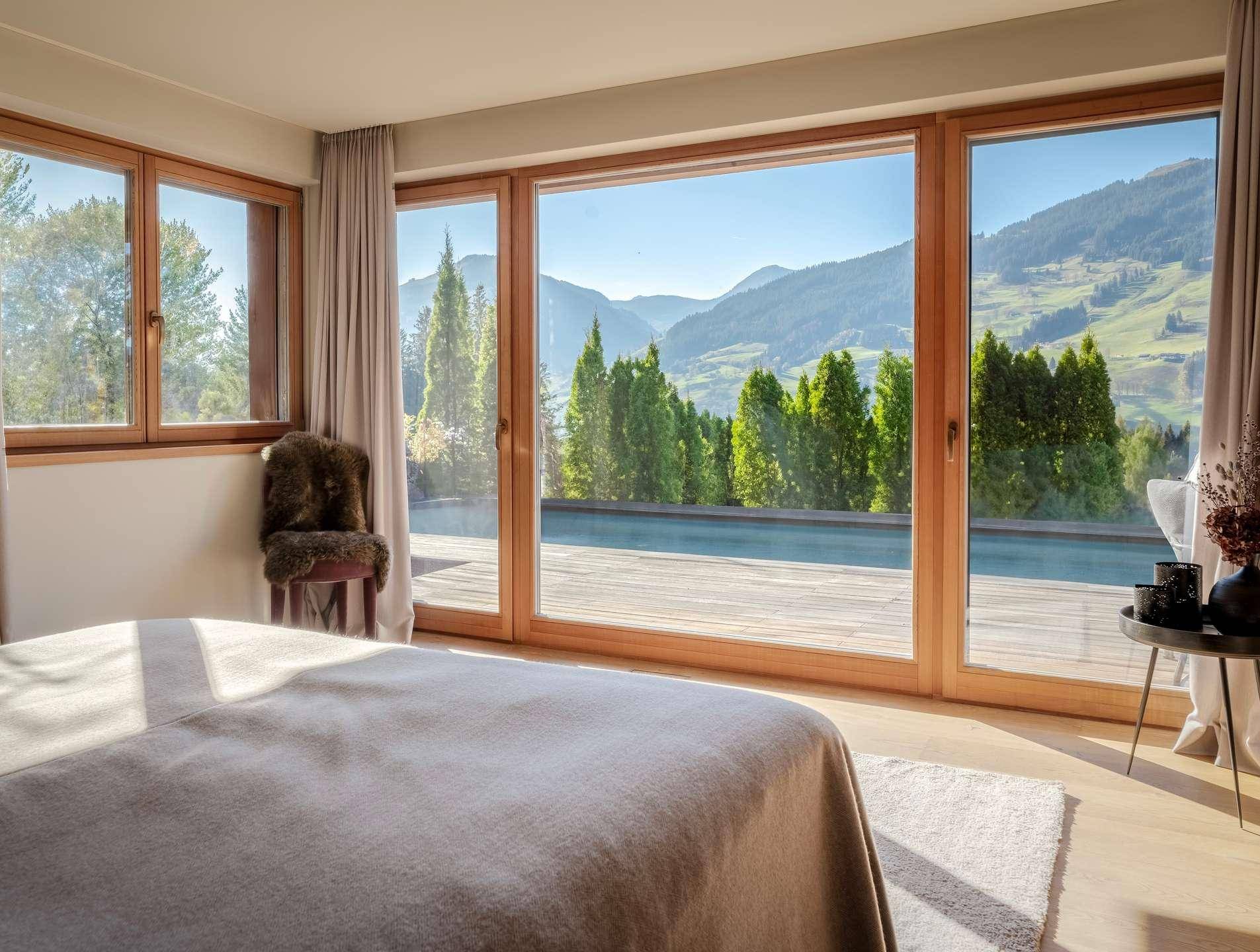 Helles Schlafzimmer mit großen Fenstern, Holzboden und direktem Blick auf die grüne Berglandschaft.