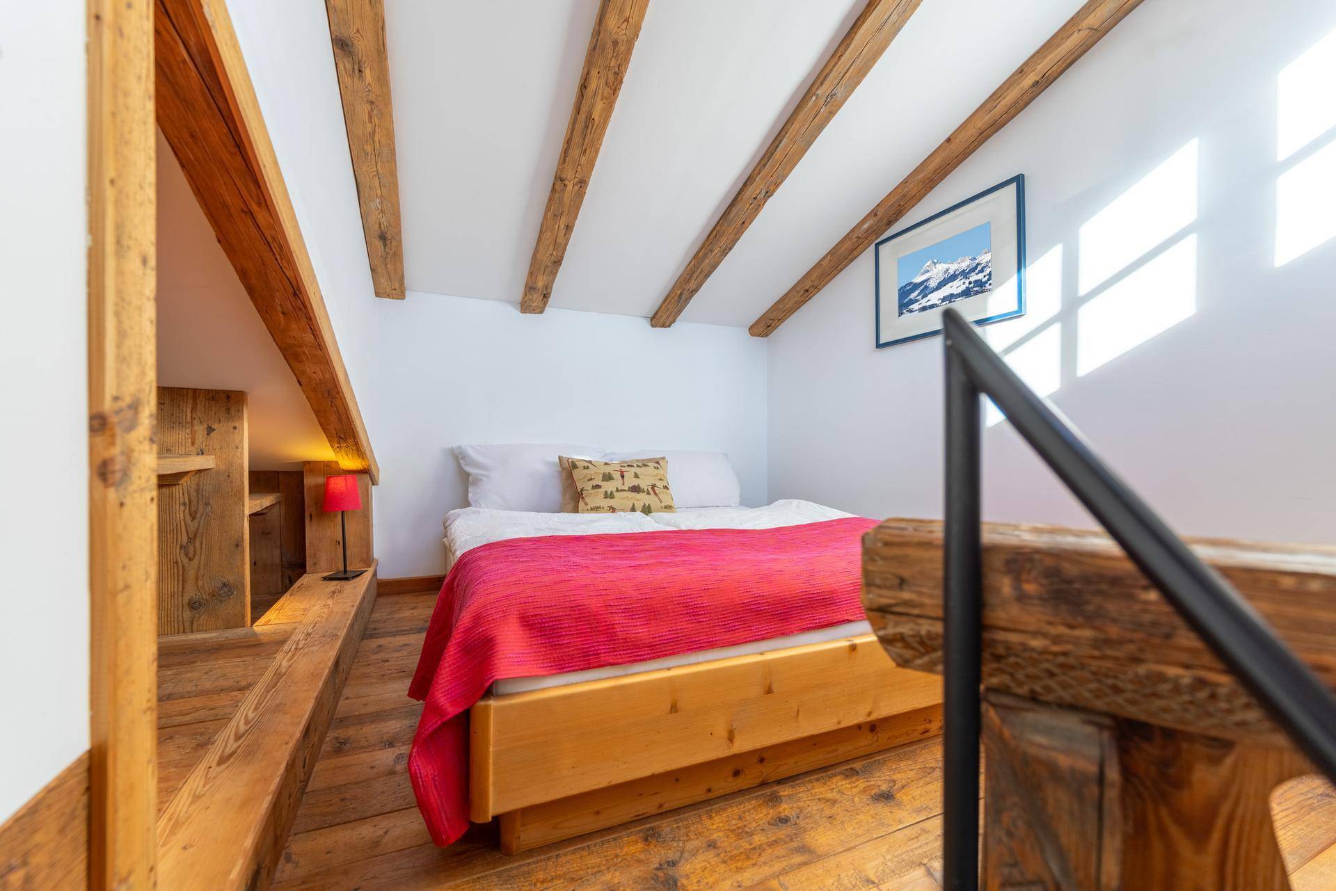 Helles Schlafzimmer im Dachgeschoss mit Holzbalken, Holzboden und schrägen Wänden.