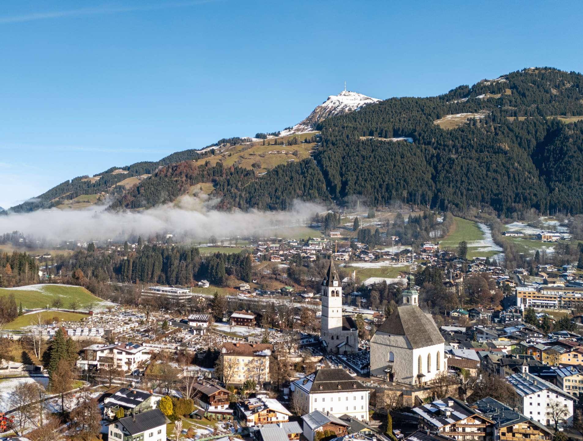 Panoramablick auf eine charmante Stadt in den Alpen mit bewaldeten Bergen im Hintergrund.