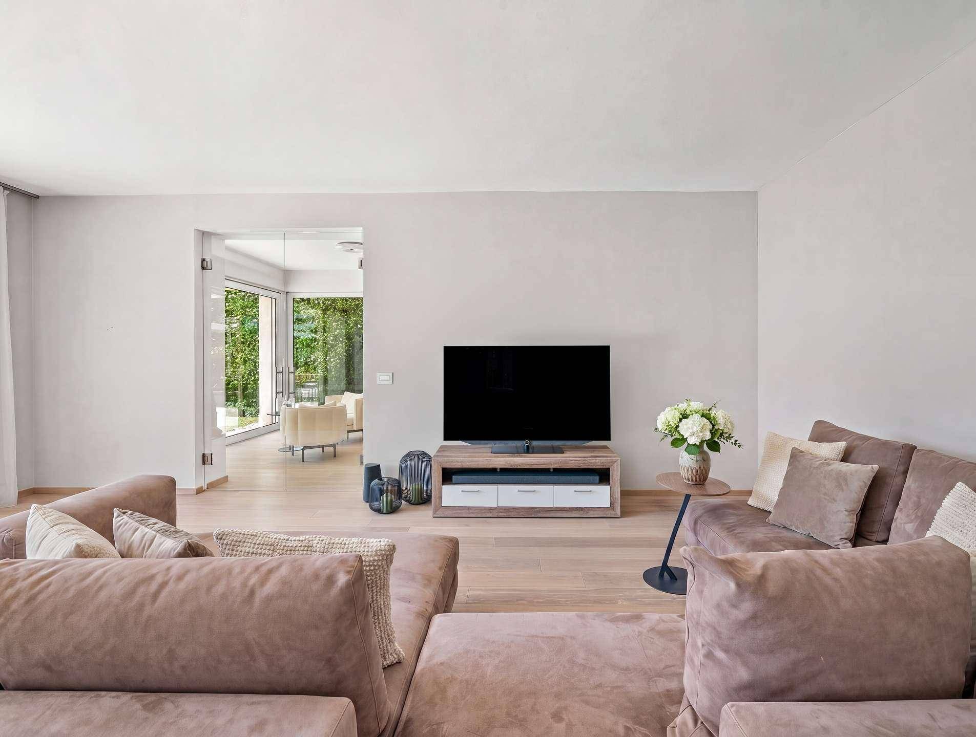 Gemütliches Wohnzimmer mit großem Sofa, Holzboden und Blick in den Garten.