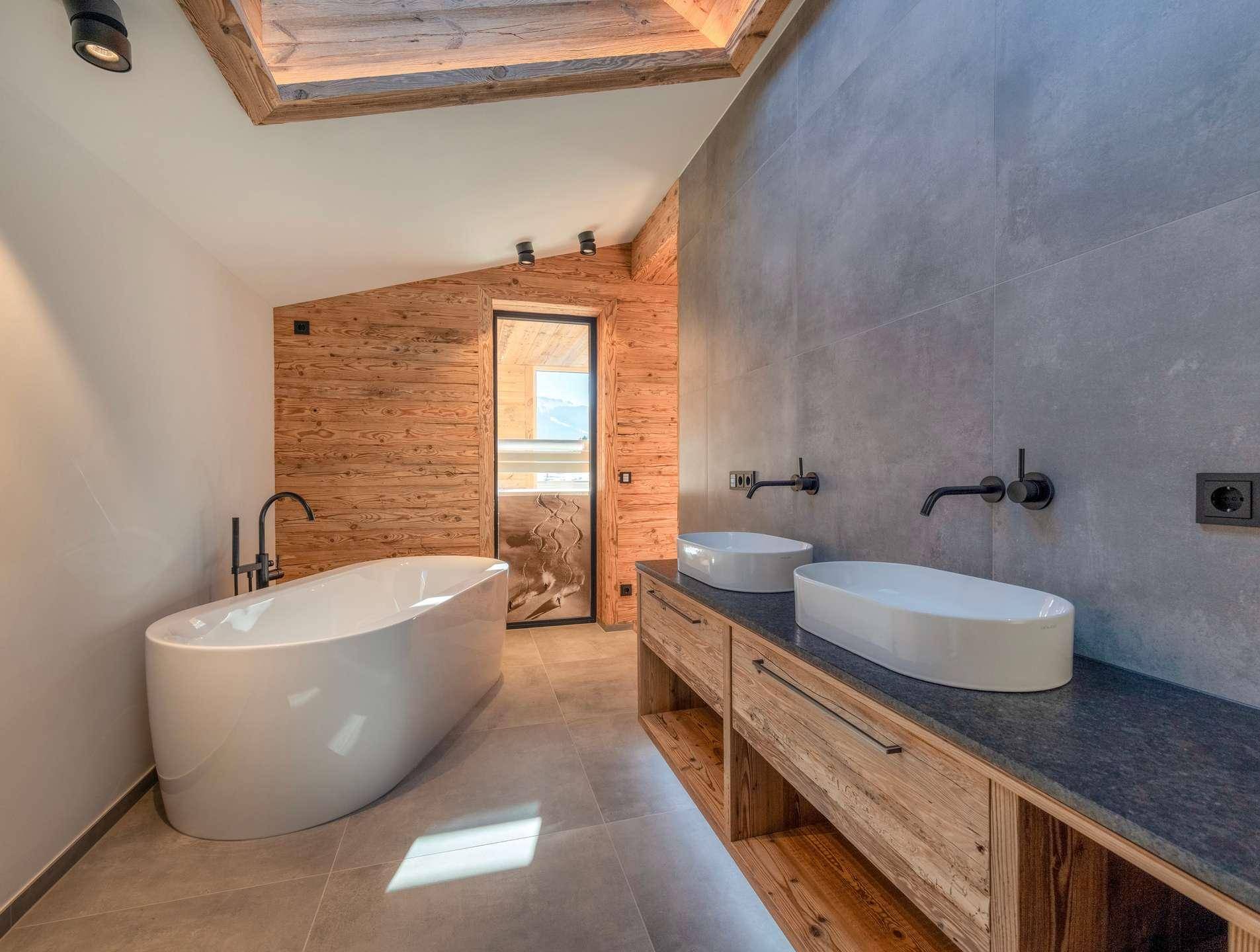 Modernes Badezimmer mit freistehender Badewanne, Doppelwaschbecken und Holzelementen unter einem Dachfenster.