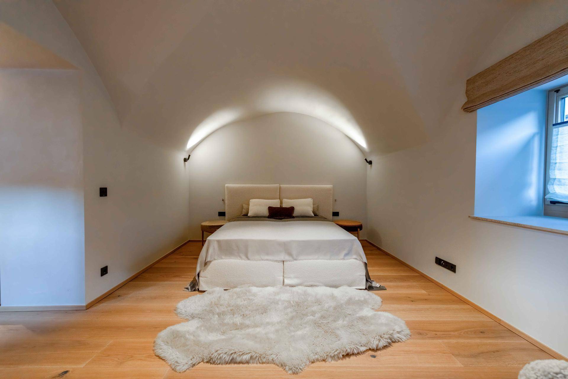 Helles Schlafzimmer mit gewölbter Decke, großem Bett und Holzboden.