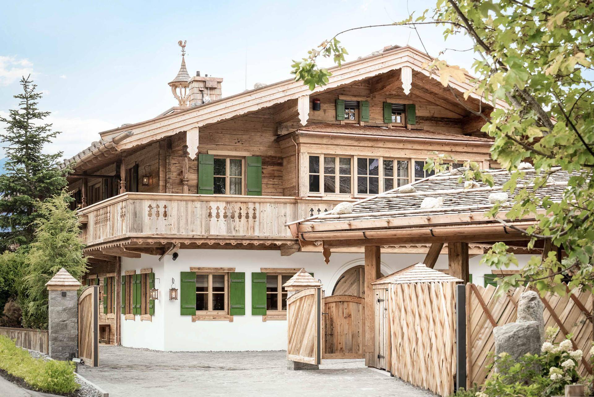 Elegantes Alpenchalet mit traditioneller Holzfassade, grünen Fensterläden und gepflastertem Eingangsbereich.