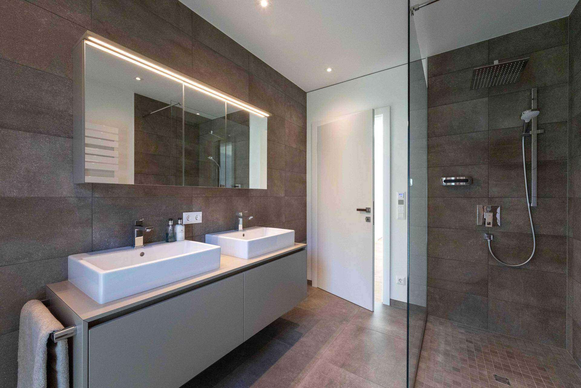 Modernes Badezimmer mit dunklen Fliesen, Doppelwaschbecken und einer geräumigen begehbaren Regendusche.