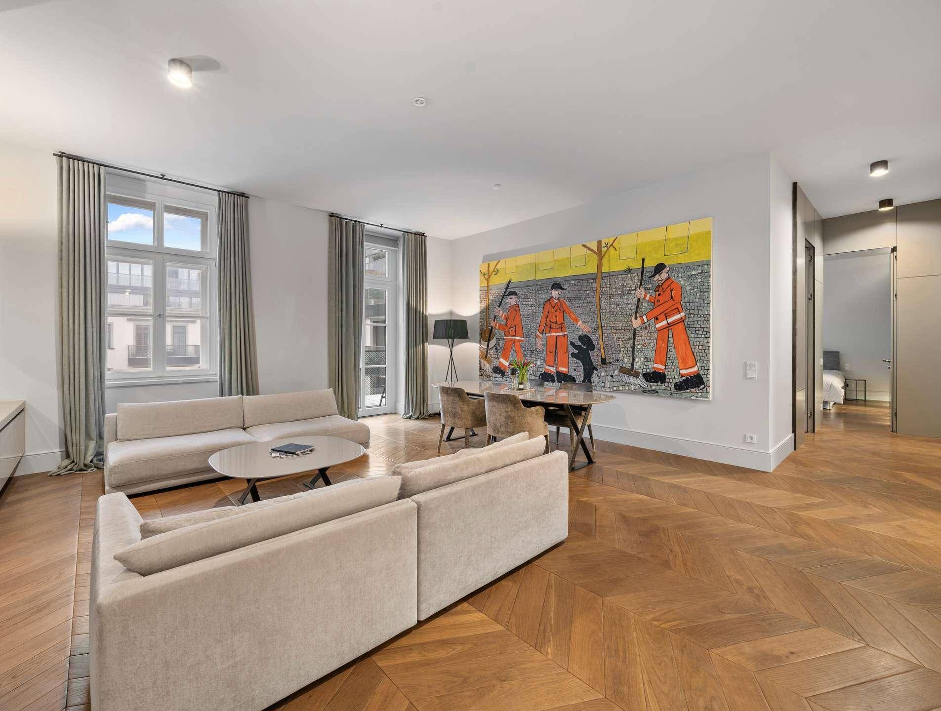 Geräumiger Wohn-Essbereich mit Fischgrätparkett, großer Kunst an der Wand und Zugang zu weiteren Räumen.