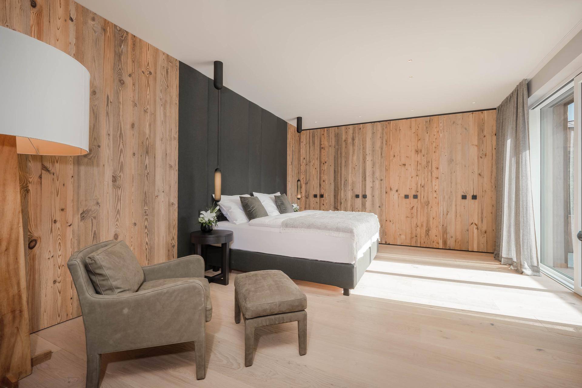 Helles Schlafzimmer mit Holzwänden, großem Bett und Zugang zu einem Balkon.