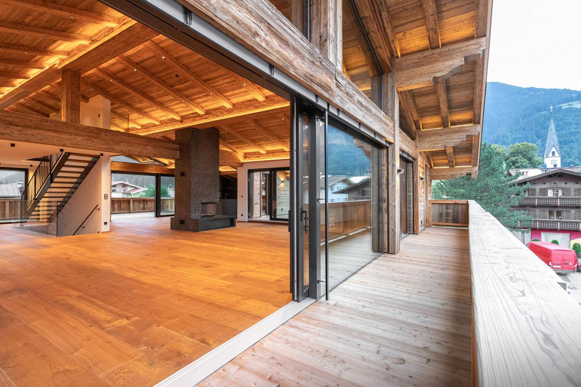 Geräumiger Wohnbereich mit Holzboden, Kamin und Zugang zu einem breiten Holzbalkon.