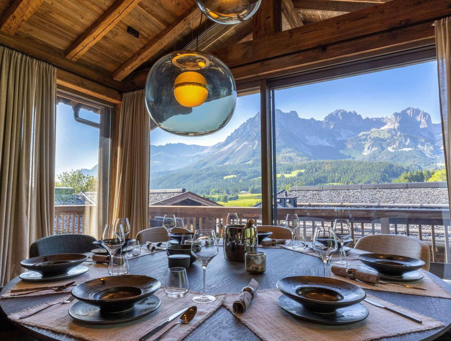 Elegantes Esszimmer mit großem Holztisch und atemberaubendem Bergblick durch Panoramafenster.