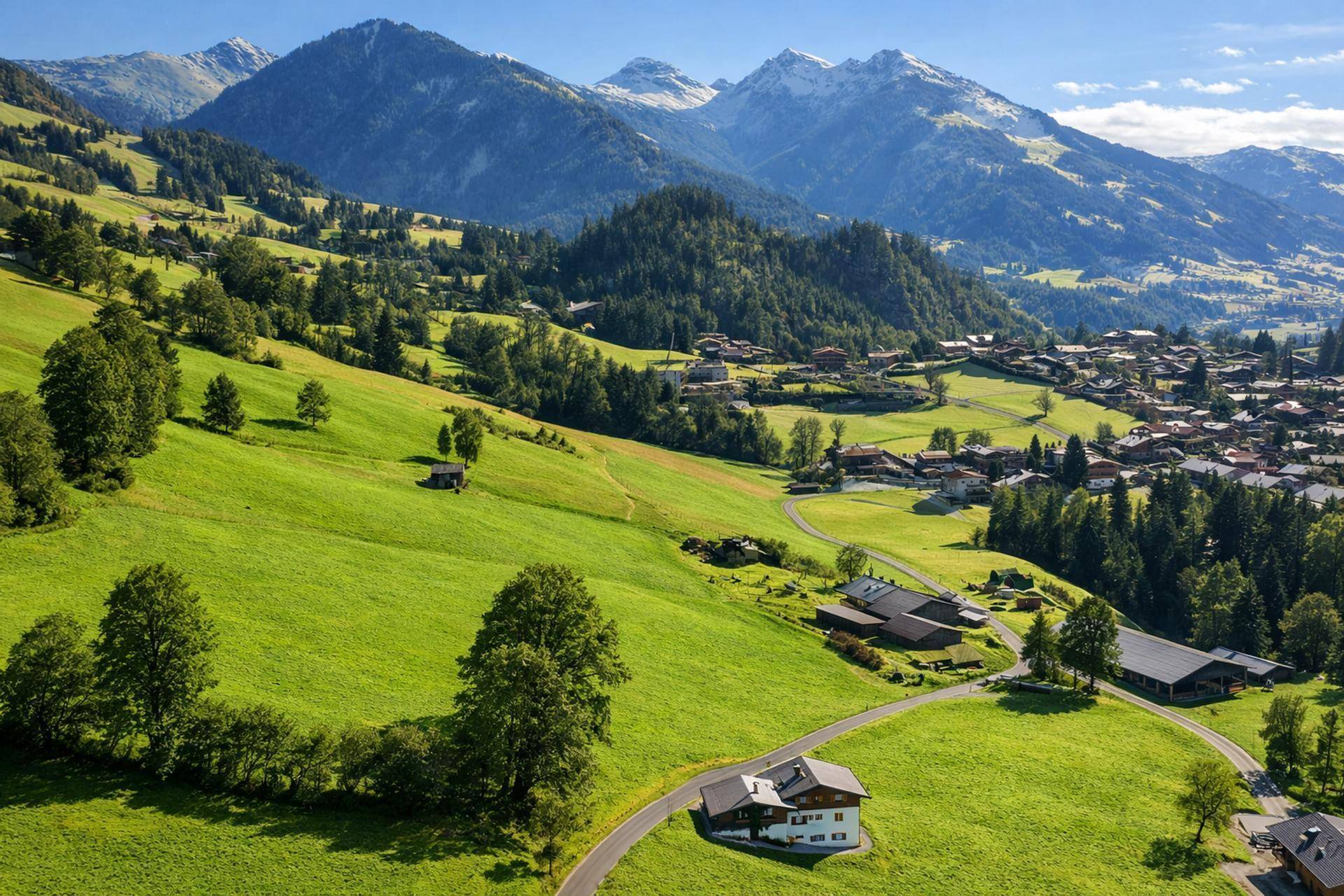 Luftaufnahme eines Hauses auf einem grünen Hügel mit kurvenreicher Zufahrt und weitem Bergblick.