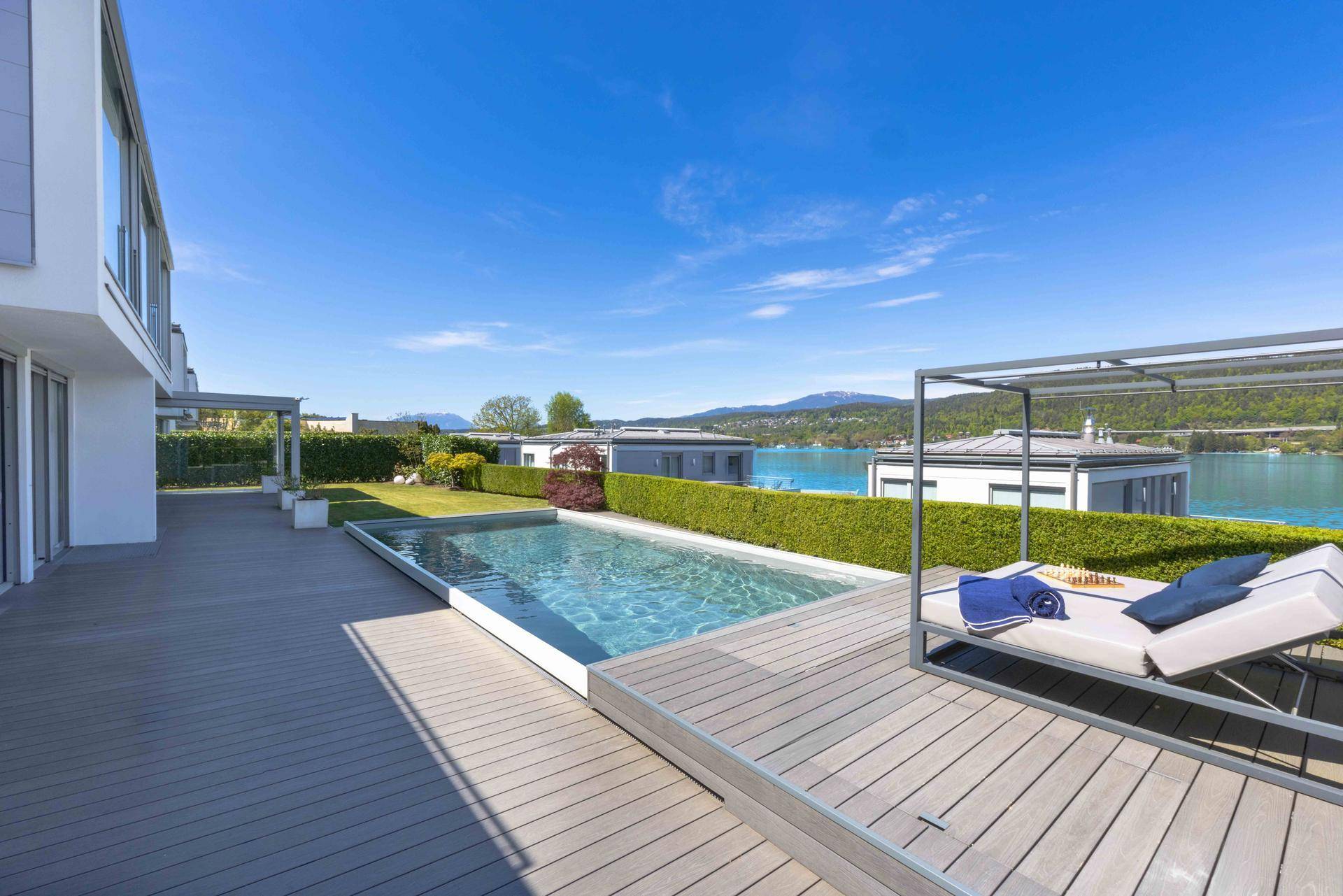 Großzügiger Poolbereich mit Holzdeck, Sonnenliegen und weitem Blick auf den See.