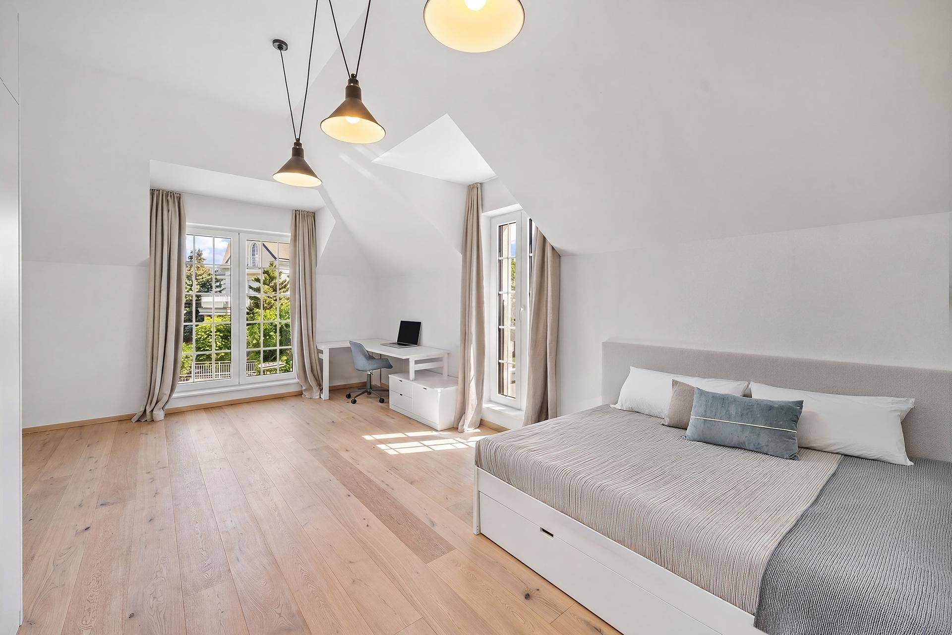 Helles Schlafzimmer mit Holzboden, Schreibtisch und großen Fenstern im Dachgeschoss.