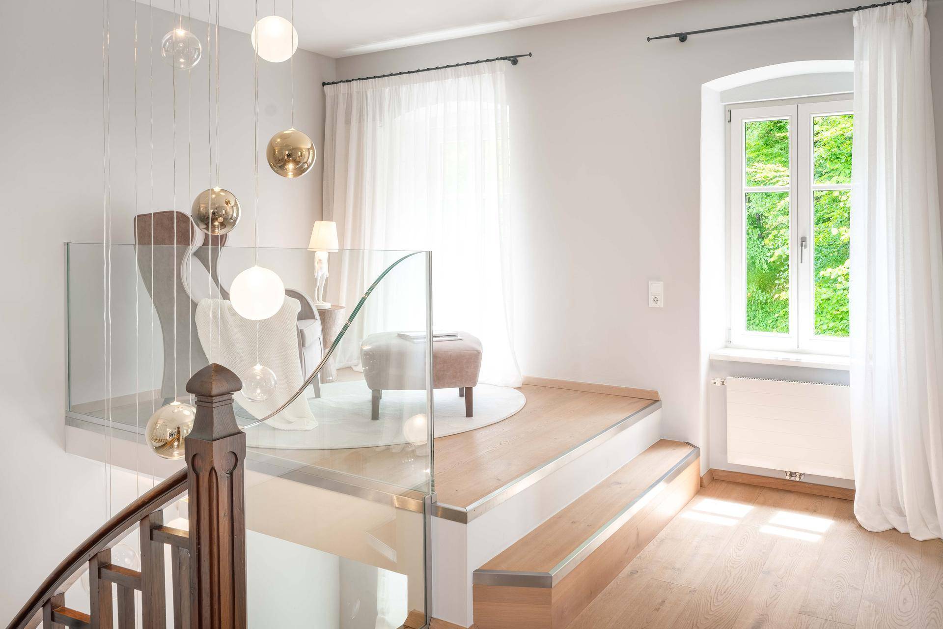 Heller Treppenabsatz mit moderner Glasbrüstung, Holzboden und dekorativen Hängelampen.