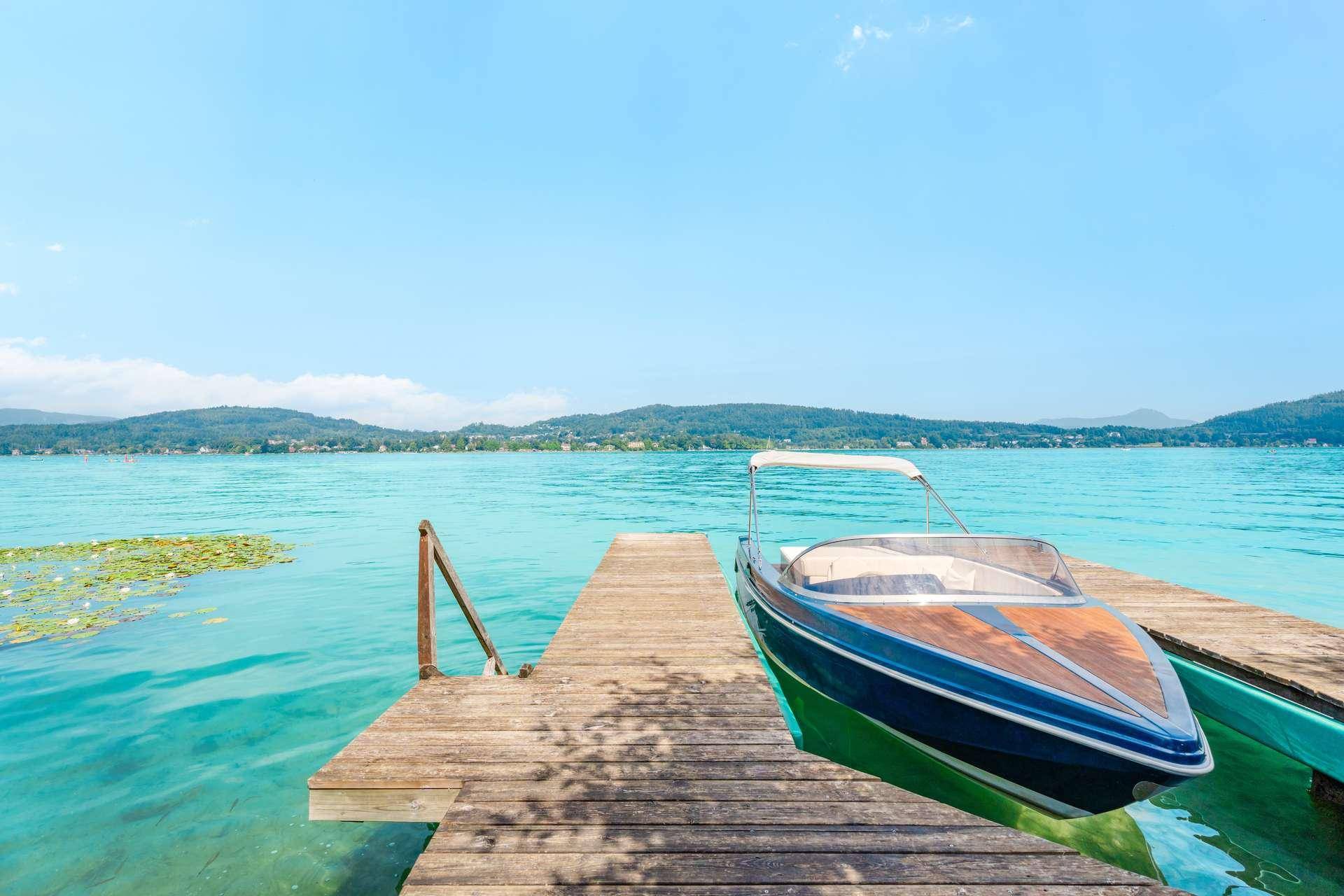 Ein Motorboot liegt an einem Holzsteg im klaren, türkisfarbenen See unter strahlend blauem Himmel.