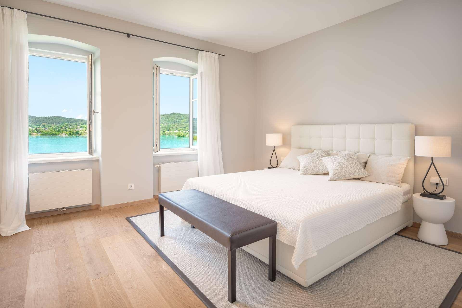 Geräumiges Schlafzimmer mit Seeblick, großen Fenstern und hellem Holzfußboden.