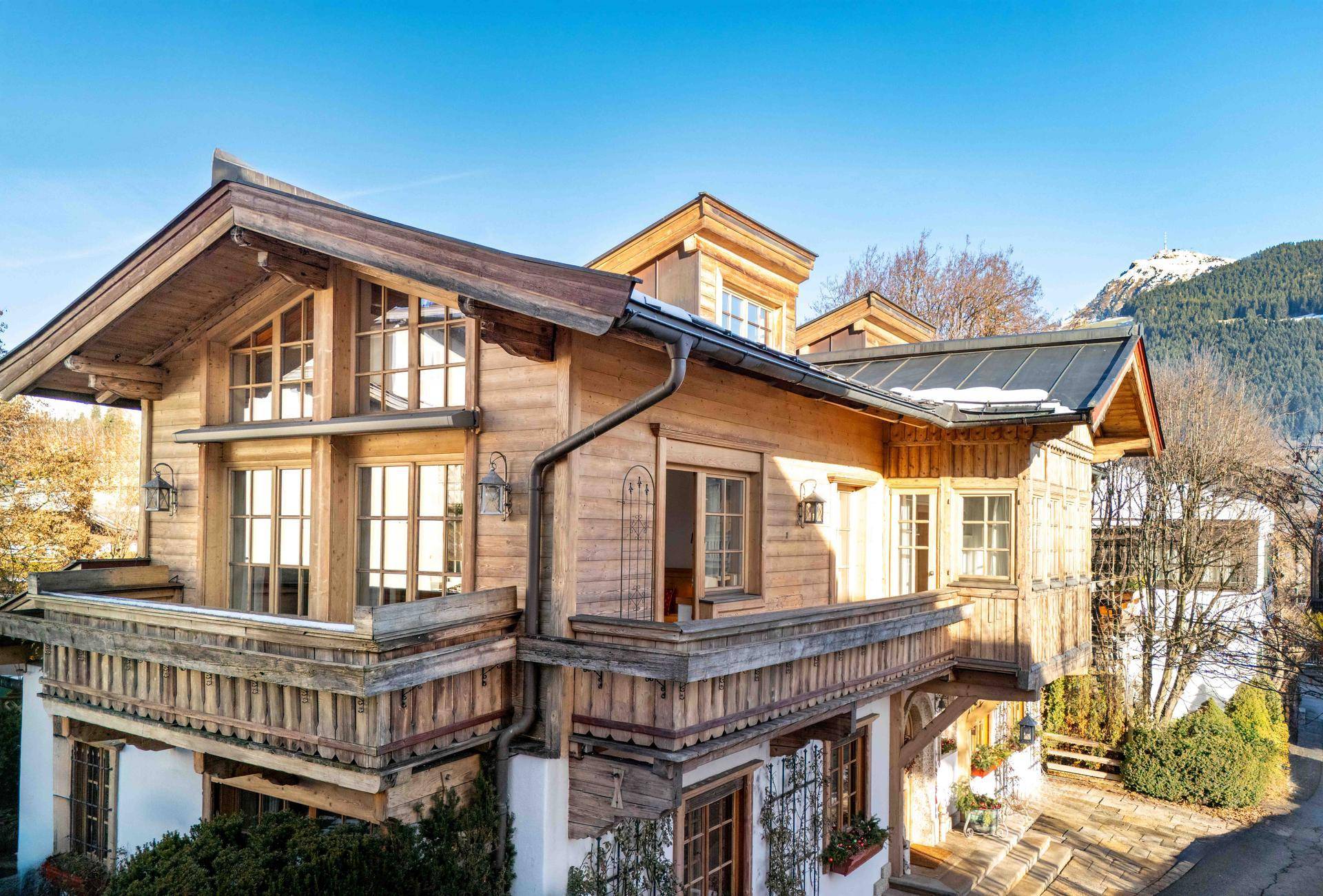 Traditionelles Holzhaus im alpinen Stil mit mehreren Balkonen und Bergblick unter blauem Himmel.