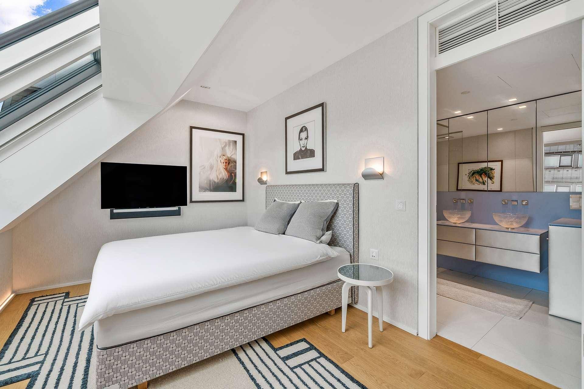 Gemütliches Schlafzimmer mit Dachfenster, Holzboden und direktem Zugang zum modernen Badezimmer.