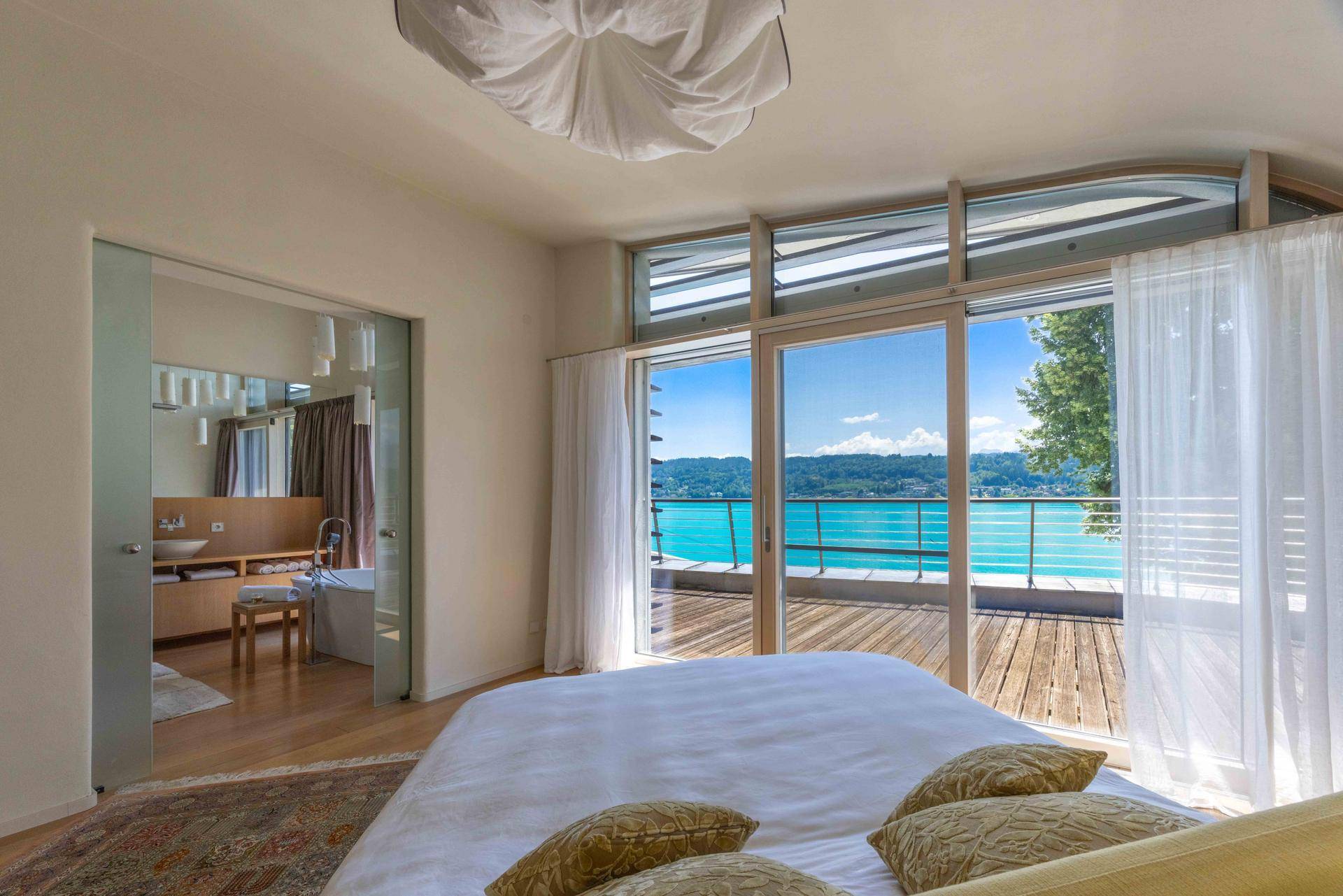 Helles Schlafzimmer mit Holzboden, Seeblick und direktem Zugang zum Balkon sowie zum Bad.