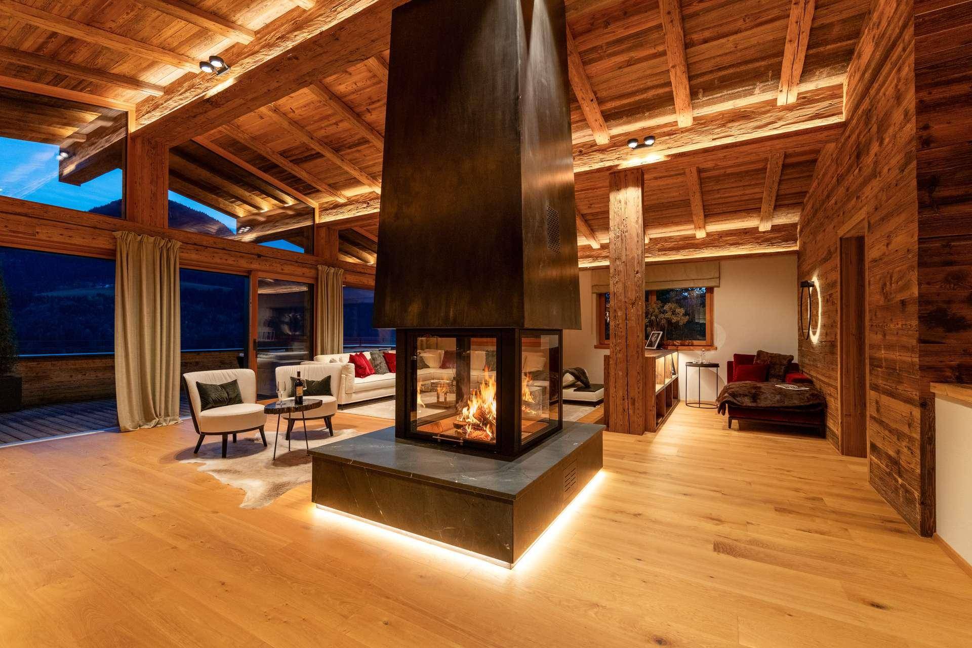 Gemütliches Wohnzimmer mit zentralem Kamin, Holzbalkendecke und indirekter Beleuchtung, ideal zum Entspannen.