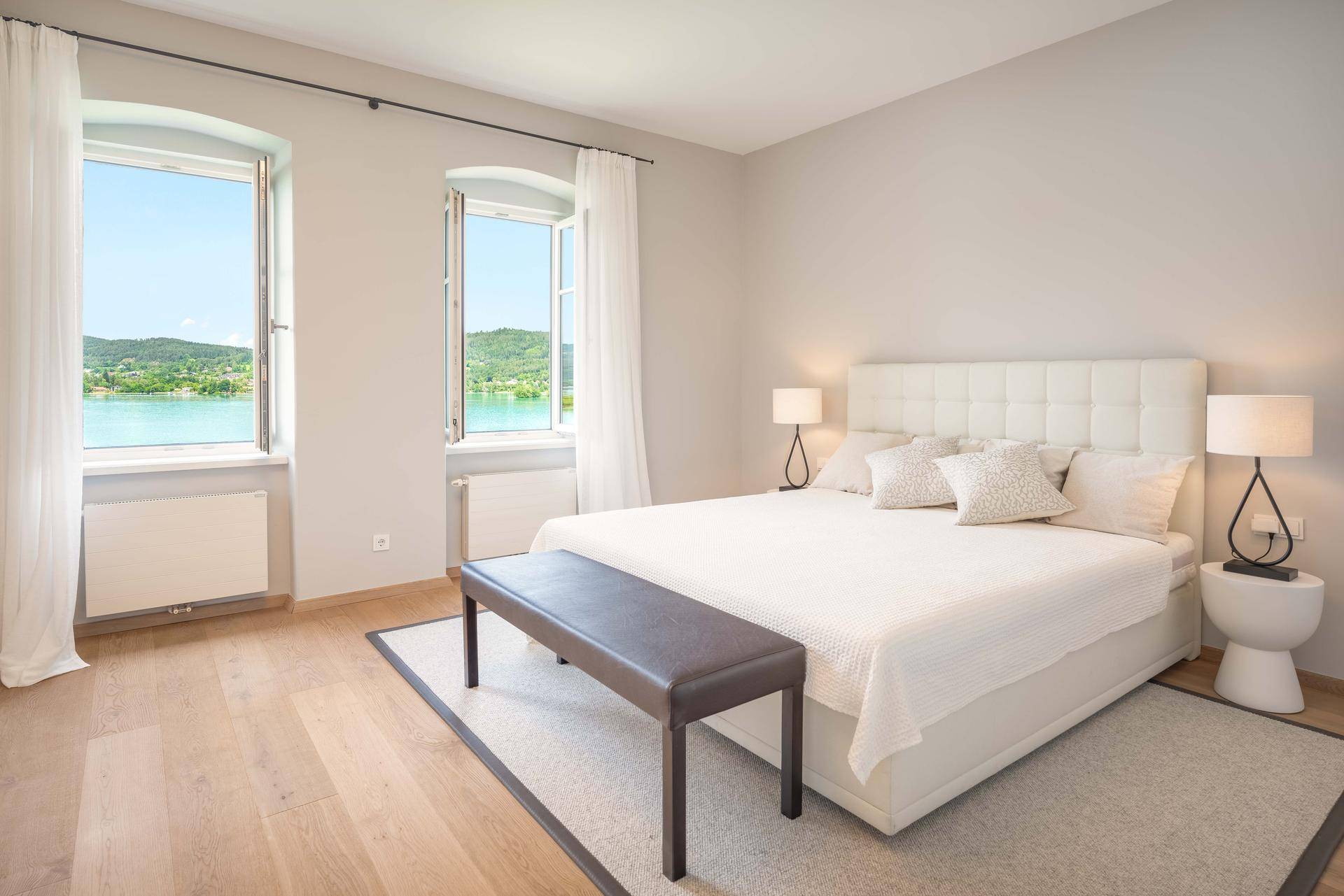 Helles Schlafzimmer mit Seeblick, großen Fenstern und modernem Doppelbett.