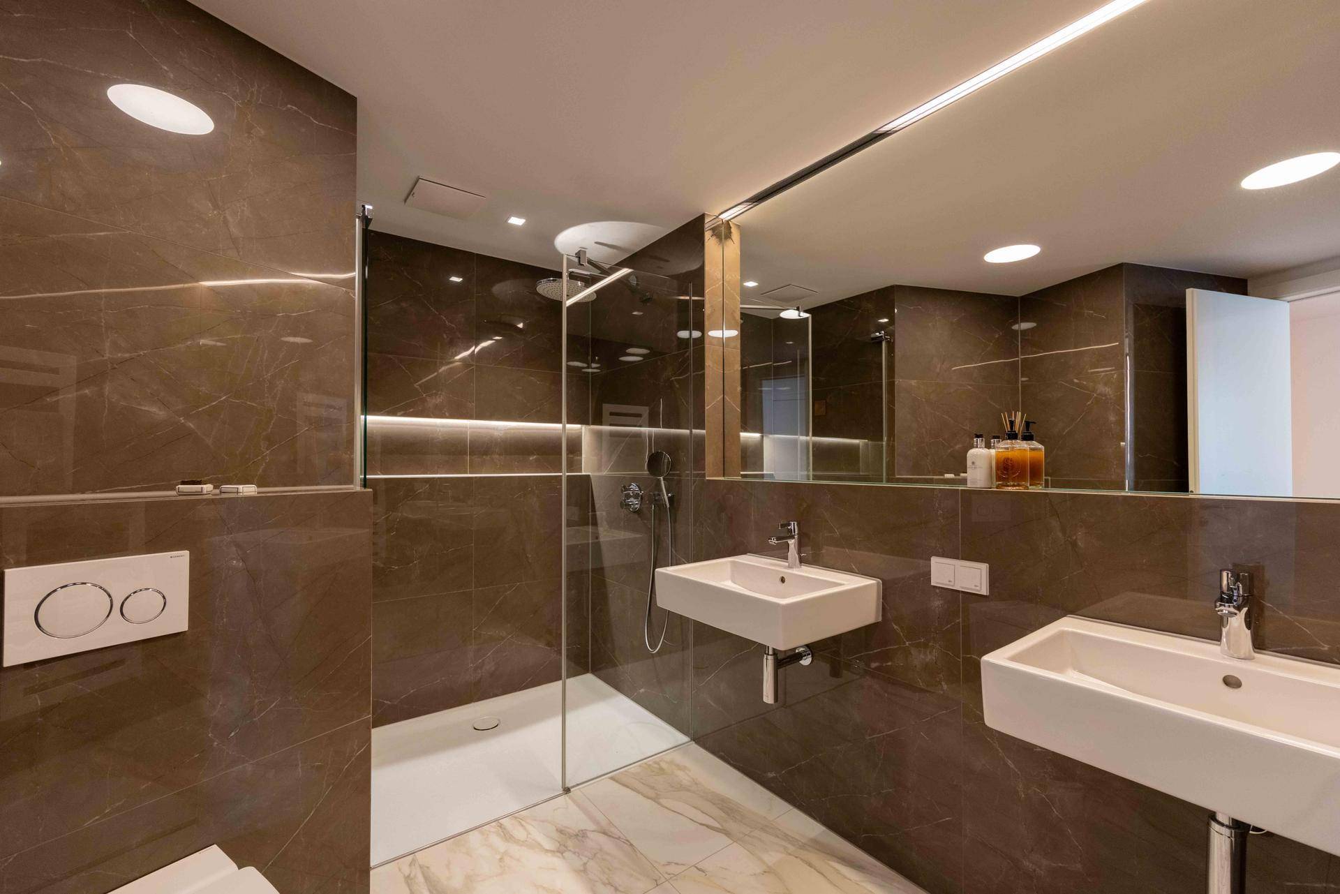 Modernes Badezimmer mit doppelten Waschbecken, großer Dusche und eleganten Marmorfliesen.