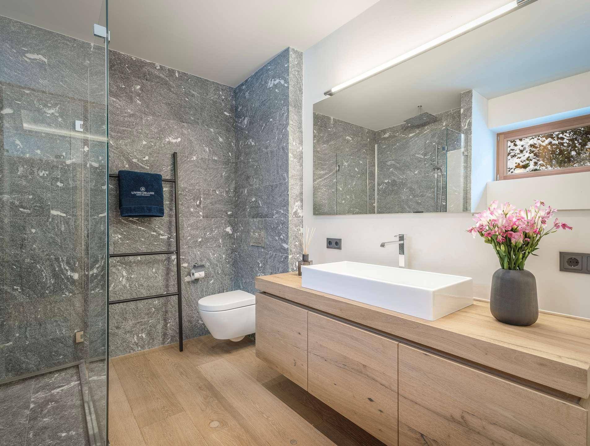 Modernes Badezimmer mit großformatigen Steinfliesen, begehbarer Dusche und Holzwaschtisch.