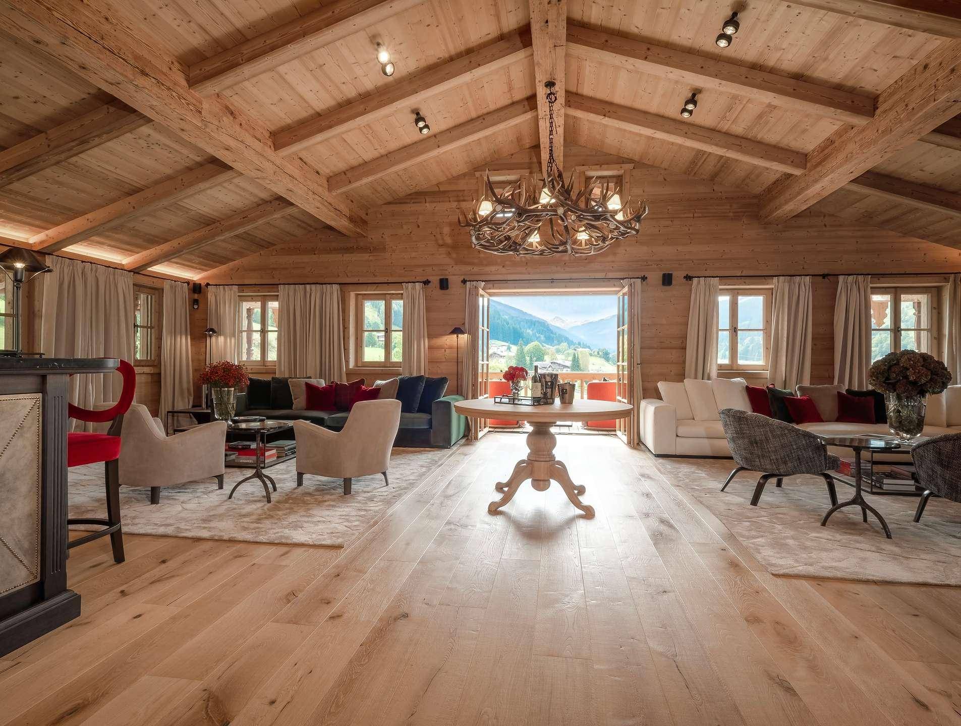 Geräumiges Wohnzimmer im Chalet-Stil mit Holzbalkendecke, Bergblick und Hirschgeweih-Kronleuchter.
