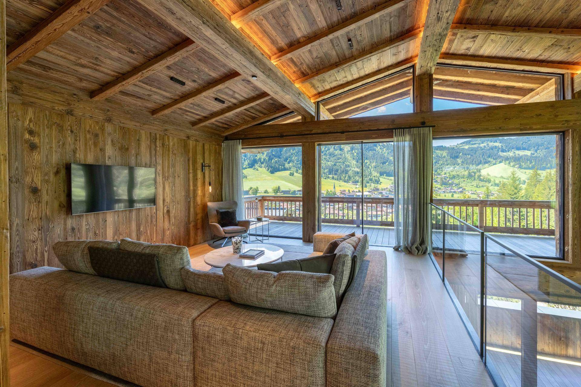 Helles Wohnzimmer mit großem Ecksofa, Holzelementen und weitem Blick auf die umliegende Berglandschaft.