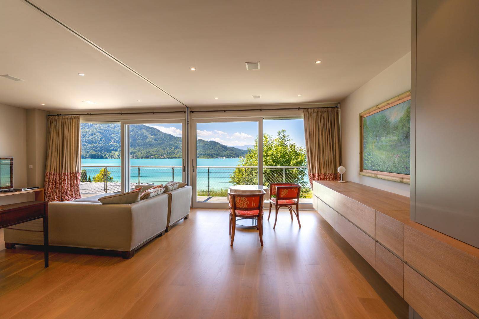 Helles Wohnzimmer mit Holzboden, großen Schiebetüren und direktem Zugang zur Terrasse mit Seeblick.