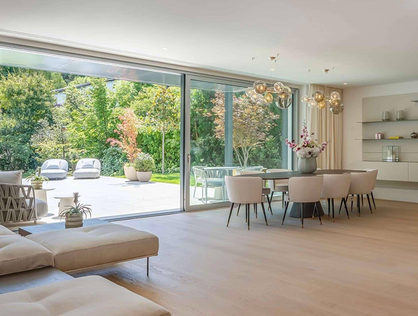 Heller Wohn- und Essbereich mit großen Schiebetüren, die zu einer Terrasse und einem grünen Garten führen.