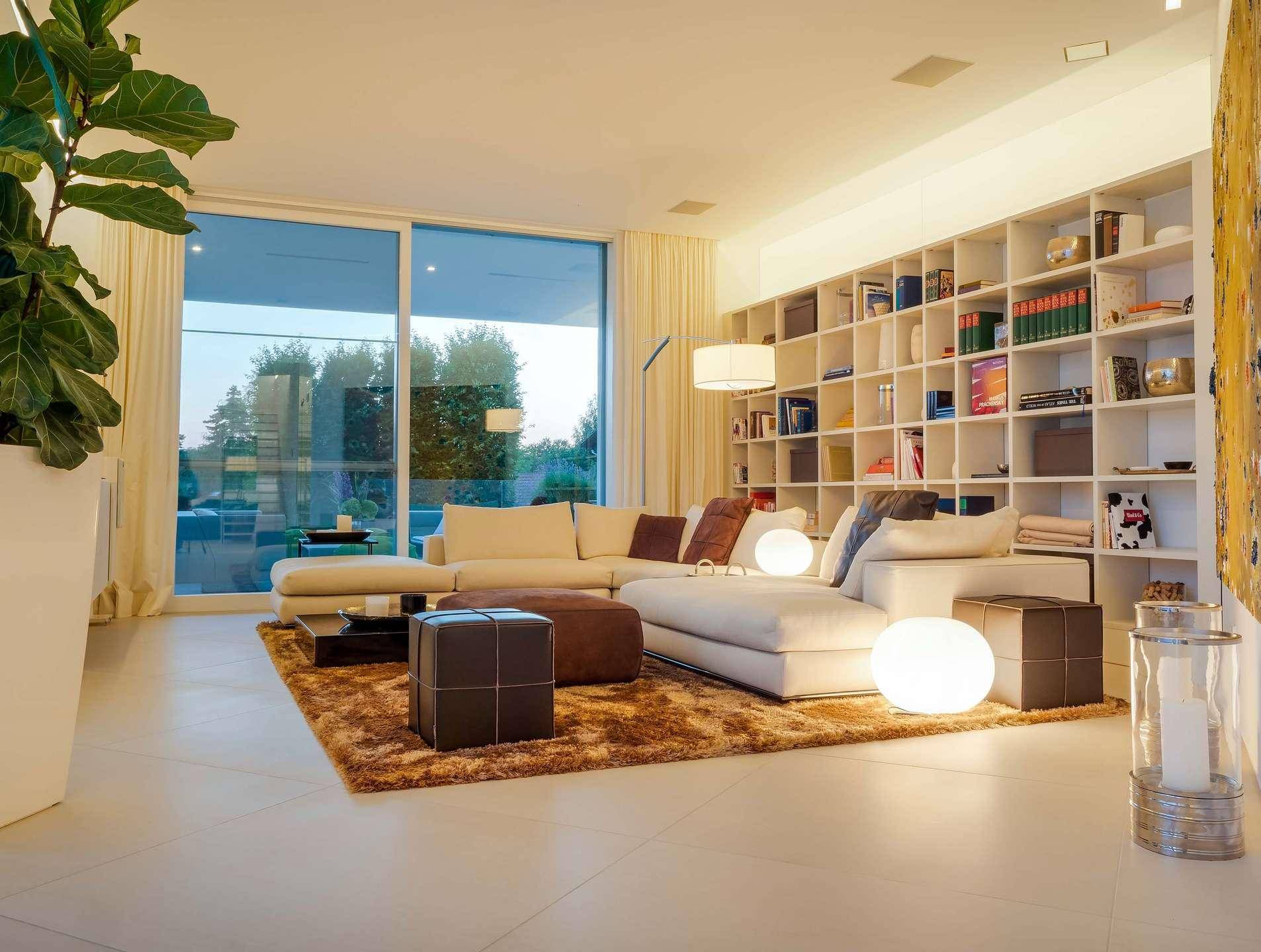 Geräumiges Wohnzimmer mit großen Fenstern, bequemer Sofalandschaft und Bücherregal.