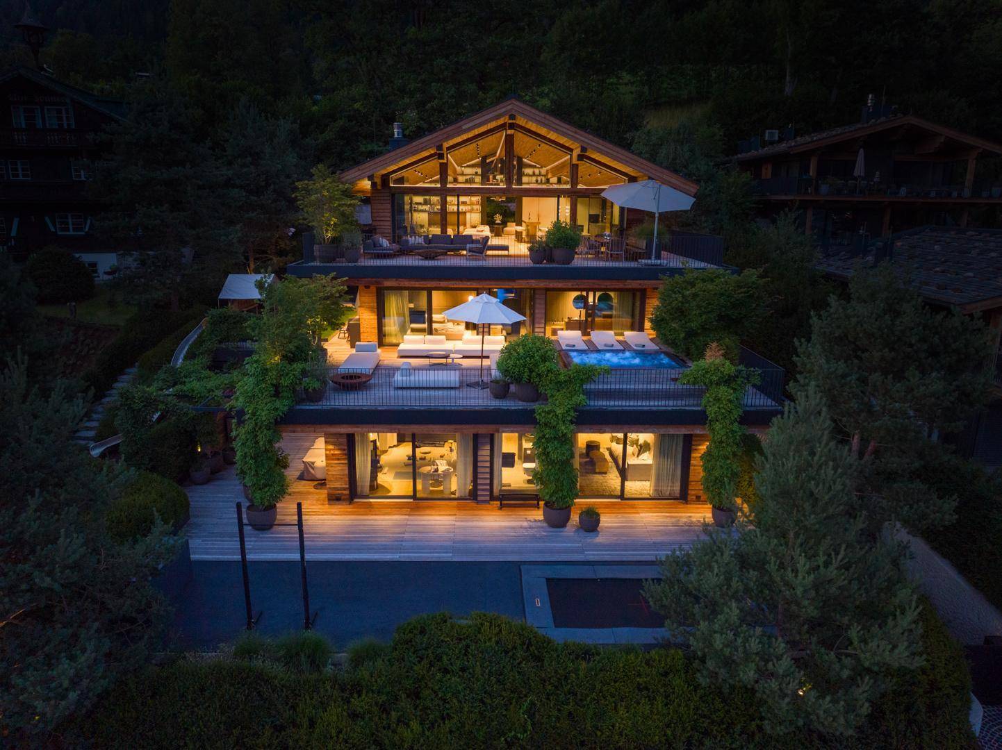 Beeindruckendes Chalet bei Nacht, beleuchtet und umgeben von üppiger Vegetation unter dem Sternenhimmel.