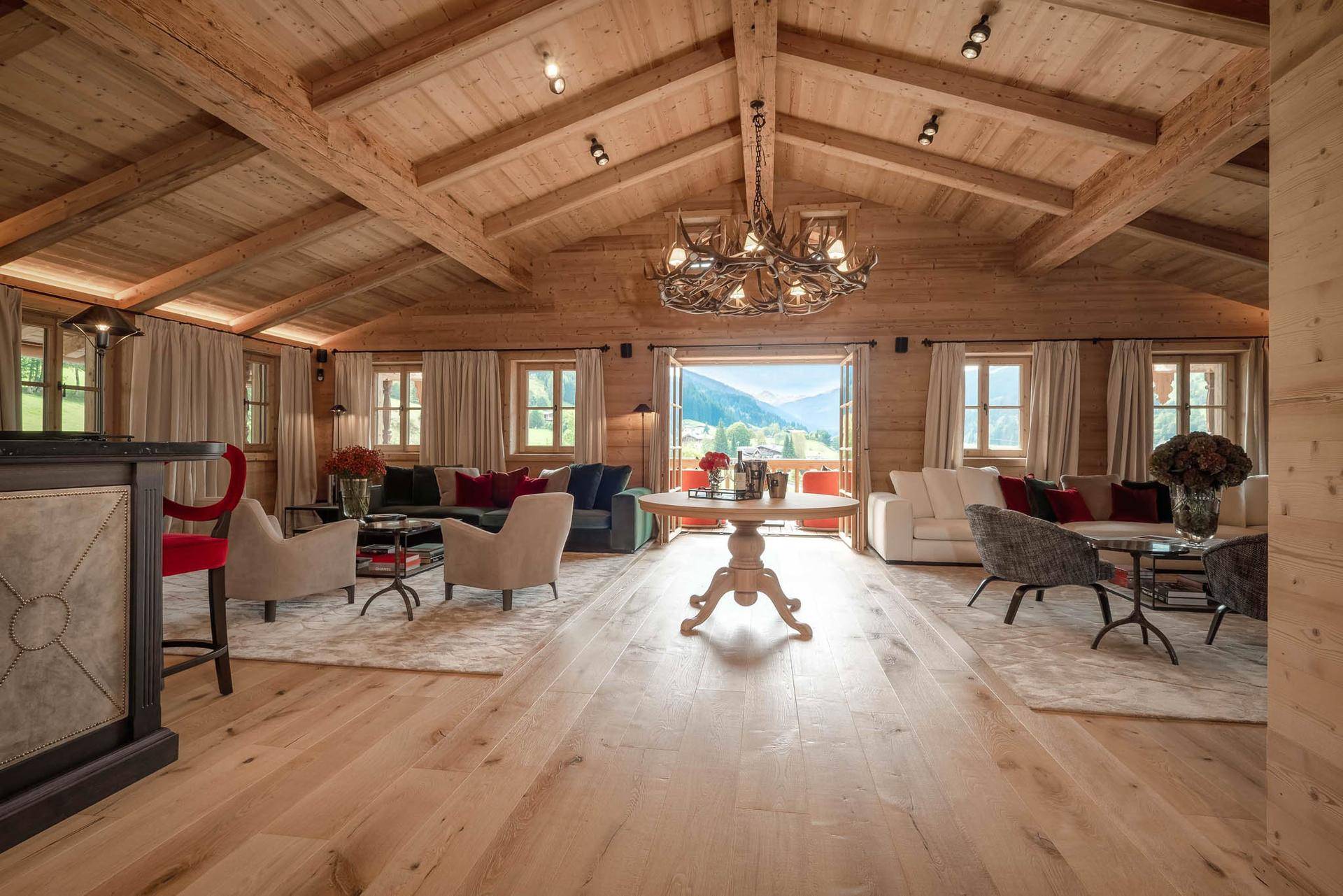 Geräumiges Wohnzimmer mit Holzbalkendecke, Hirschgeweih-Kronleuchter und Zugang zum Balkon.