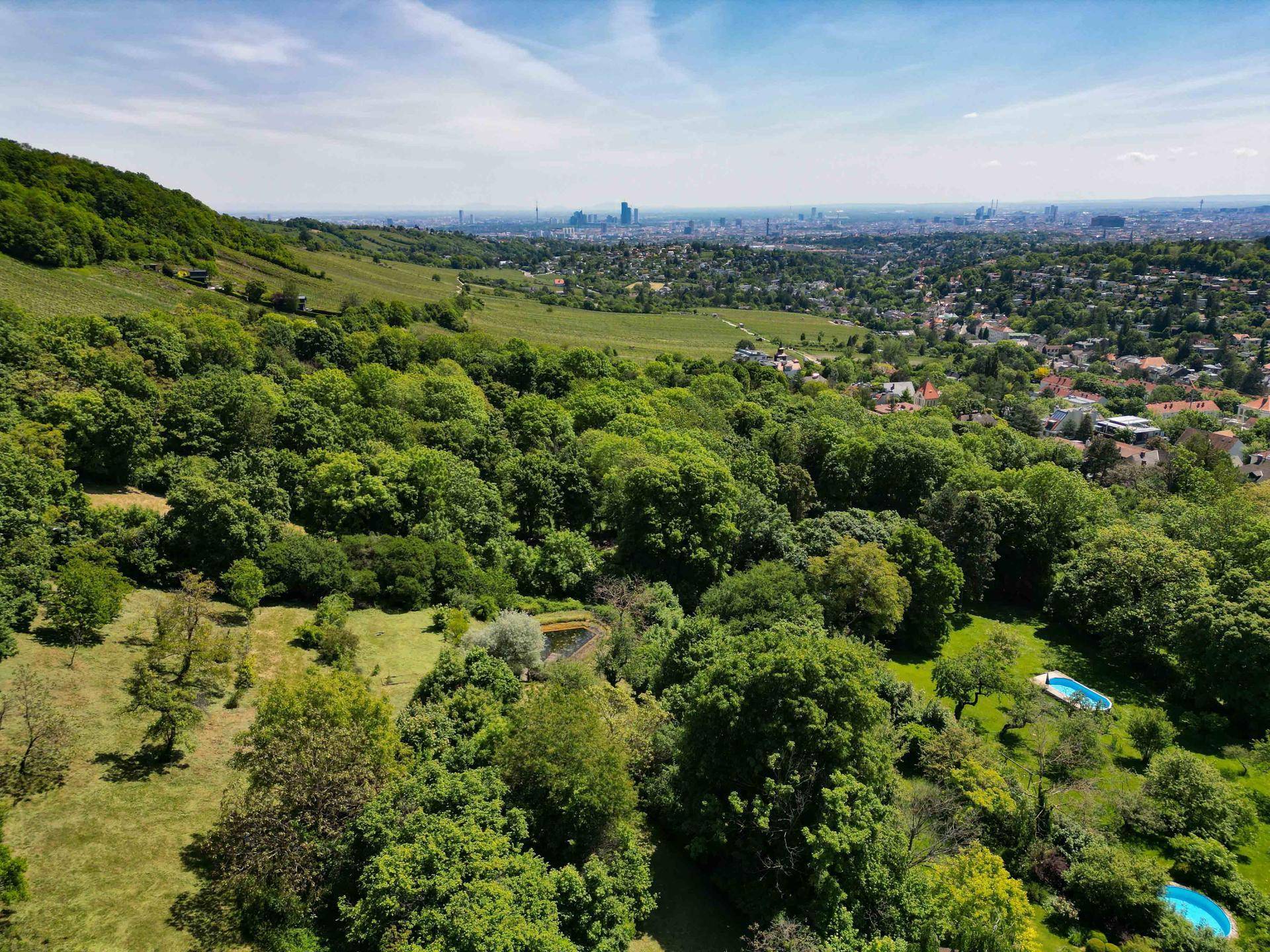Weitläufige grüne Landschaft mit Pool und Panoramablick auf die Stadt in der Ferne.