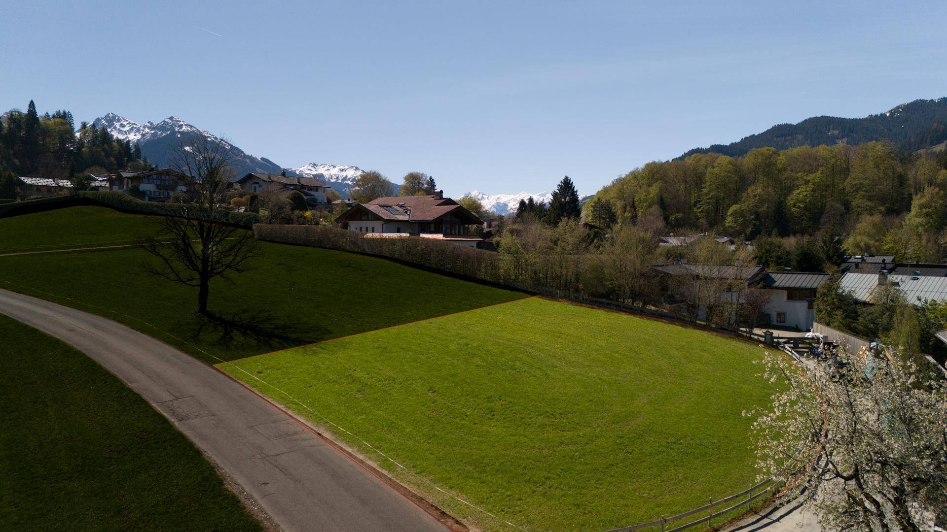 Weitläufige grüne Wiesen mit Blick auf die umliegende Berglandschaft und vereinzelte Häuser.