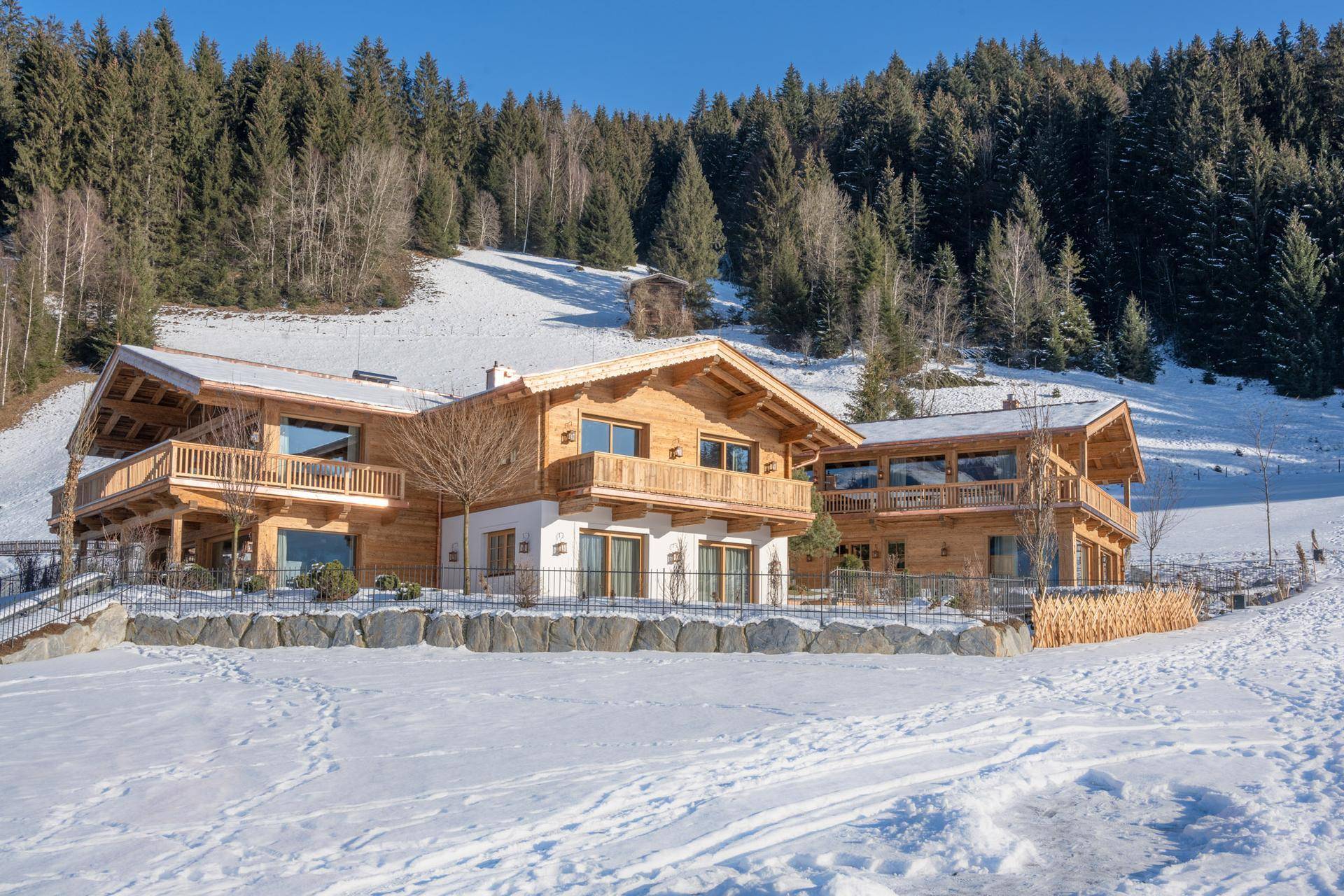 Zwei luxuriöse Chalets in alpiner Landschaft, umgeben von verschneiten Hängen und Tannenwäldern.