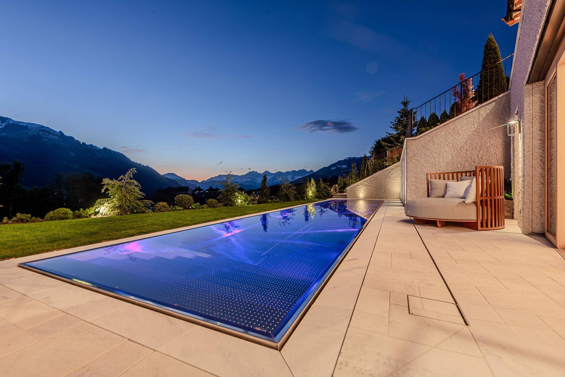 Langer, beleuchteter Pool mit atemberaubendem Bergblick und Liegebereich am Abend.