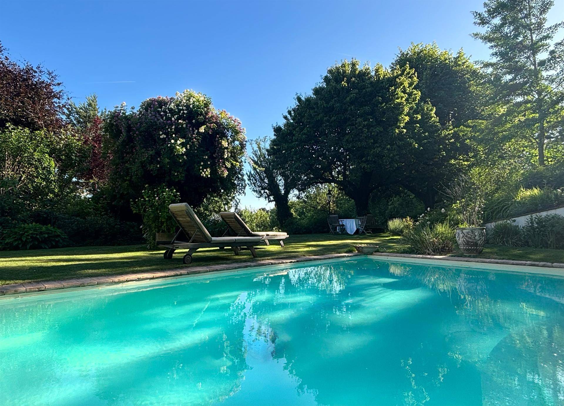 Einladender Poolbereich im Garten mit bequemen Liegestühlen und üppiger Bepflanzung.