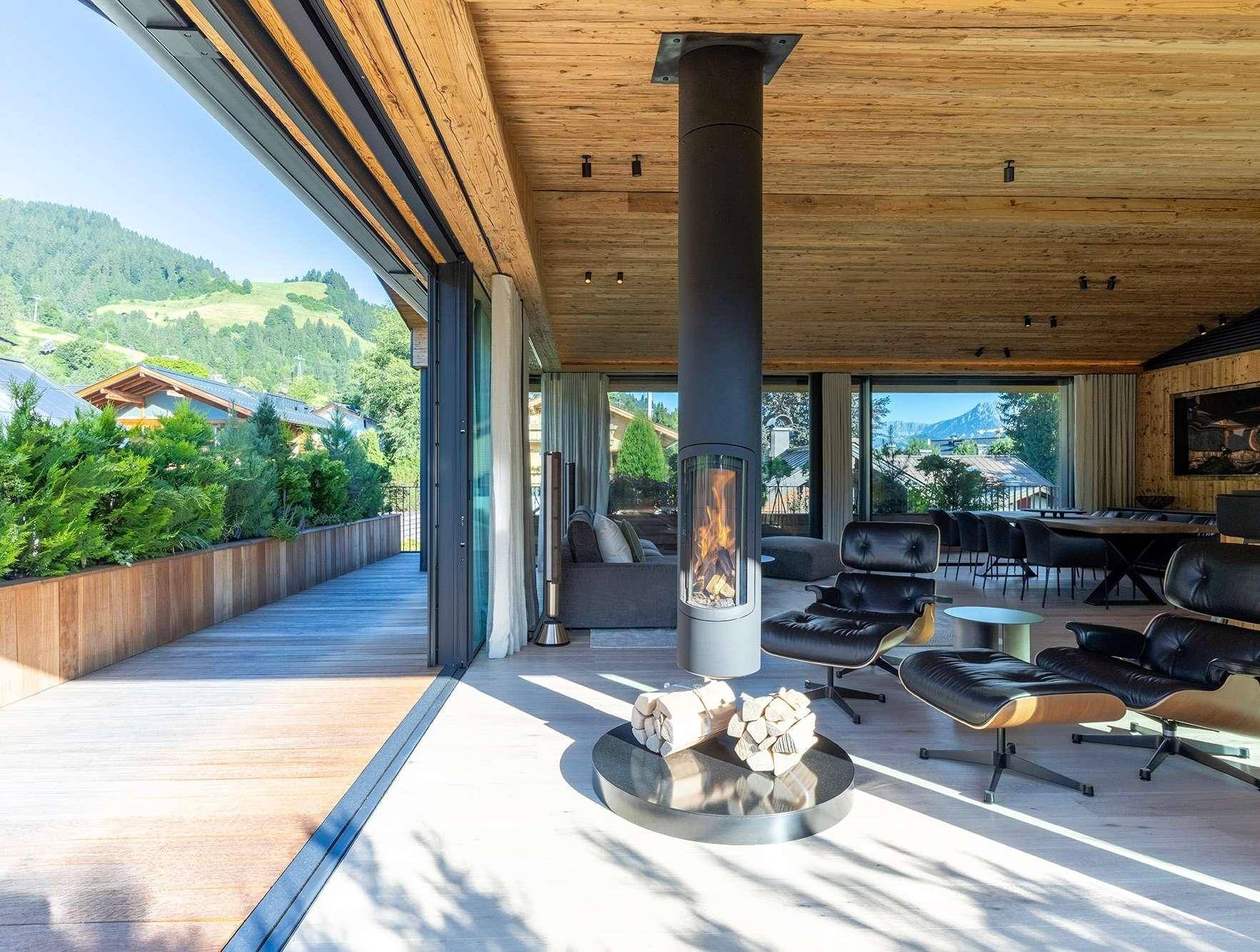 Geräumiger Wohn-Essbereich mit modernem Kamin, Holzakzenten und Zugang zu einer großen Terrasse mit Bergblick.