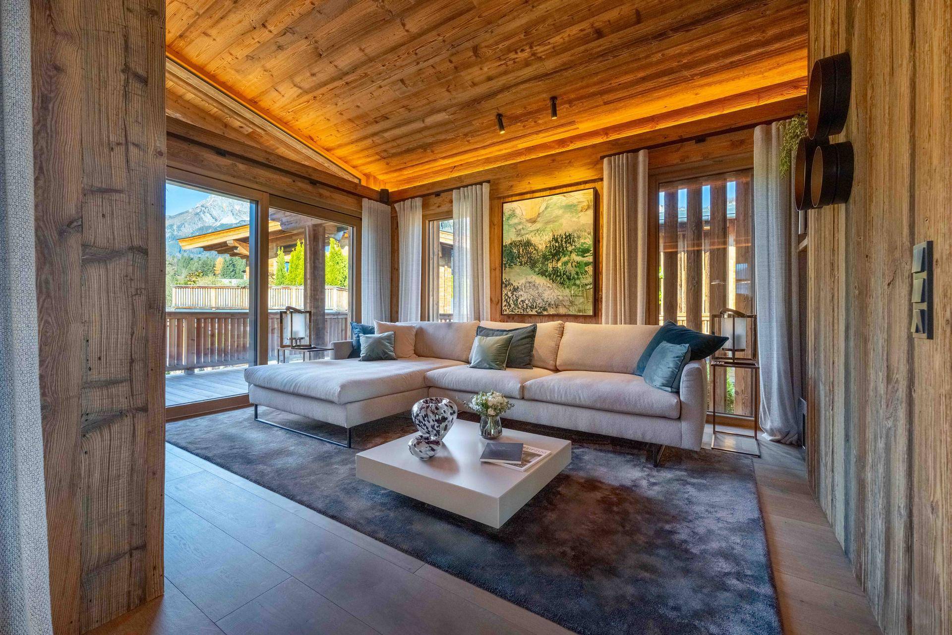 Gemütliches Wohnzimmer mit großem Sofa, Holzwänden und Zugang zu einem Balkon mit Bergblick.