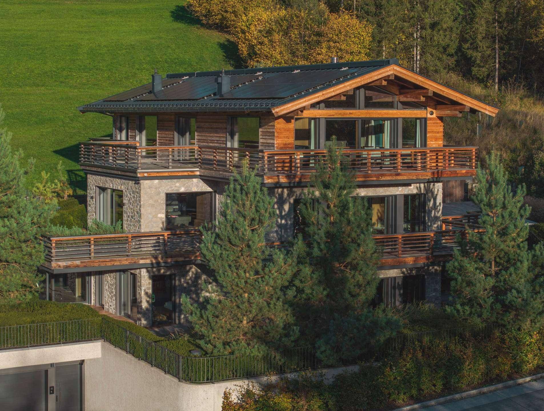 Luxuriöses Chalet mit Holzfassade, Steinelementen und mehreren Balkonen in alpiner Umgebung.