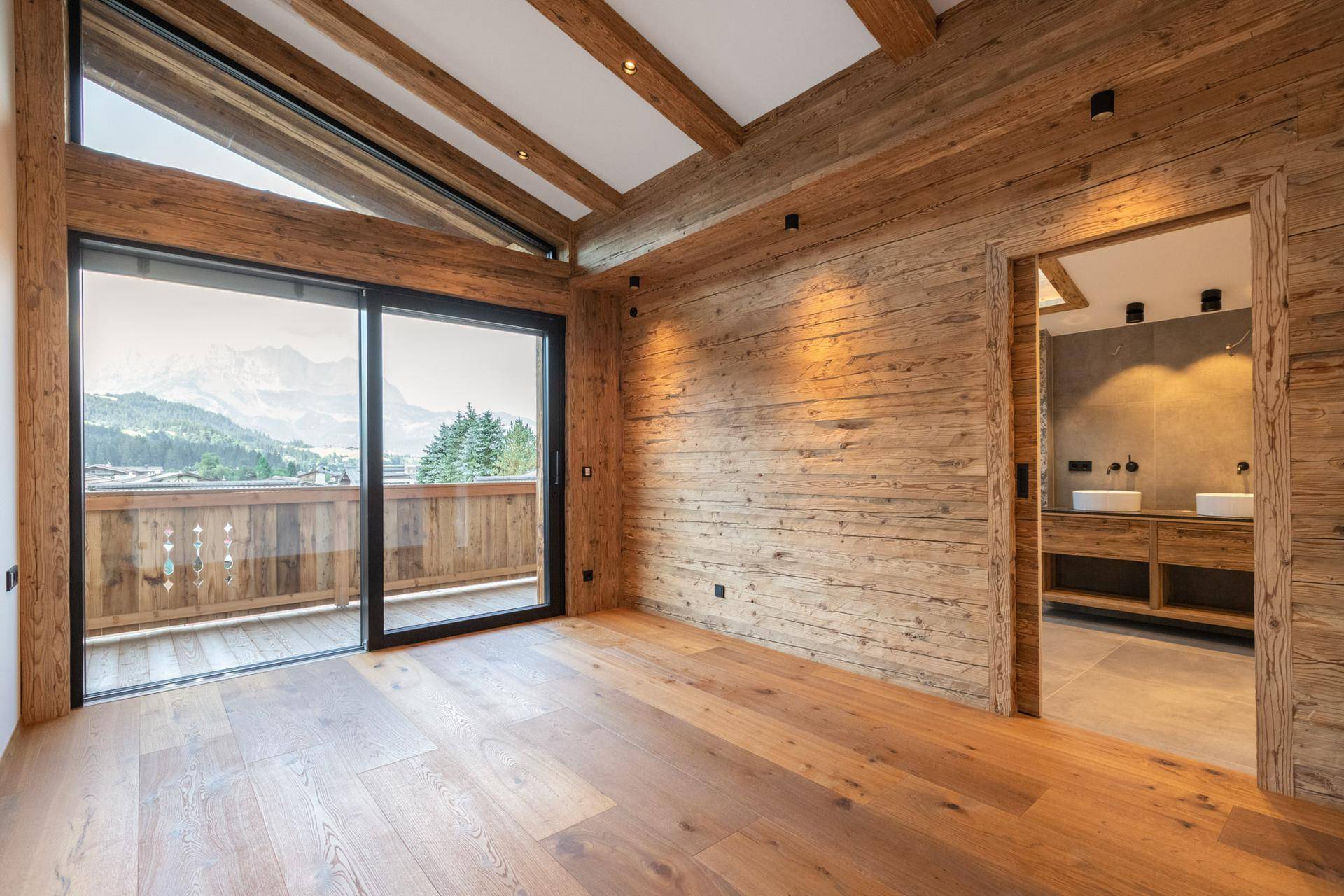 Gemütliches Schlafzimmer mit Holzwänden, Balkonzugang und Blick auf die umliegende Berglandschaft.