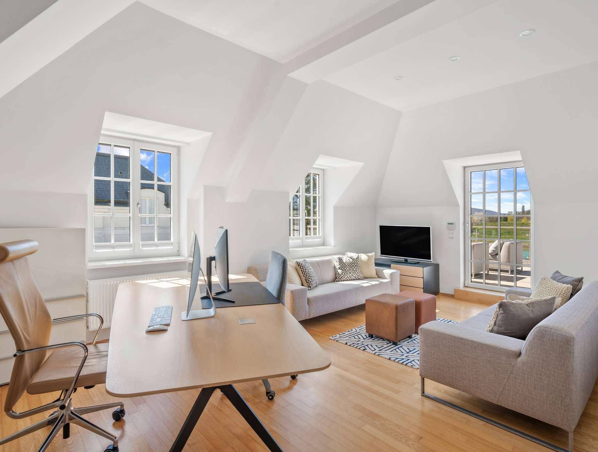 Helles Dachgeschosszimmer mit Arbeitsbereich, Sitzgelegenheiten und Blick ins Grüne.