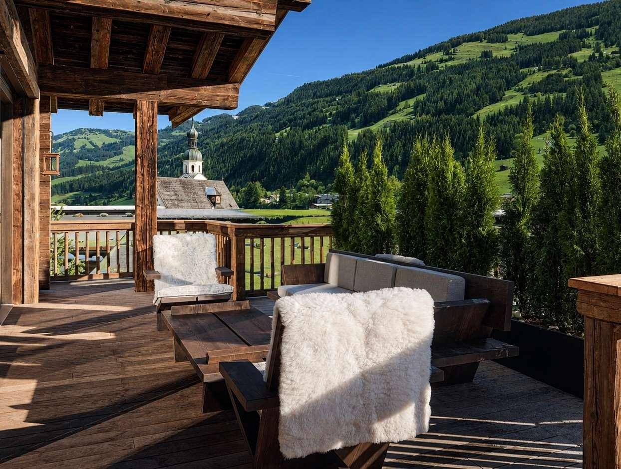 Gemütliche Holzterrasse mit Sitzgelegenheiten und weitem Blick auf die Berge und ein charmantes Dorf.