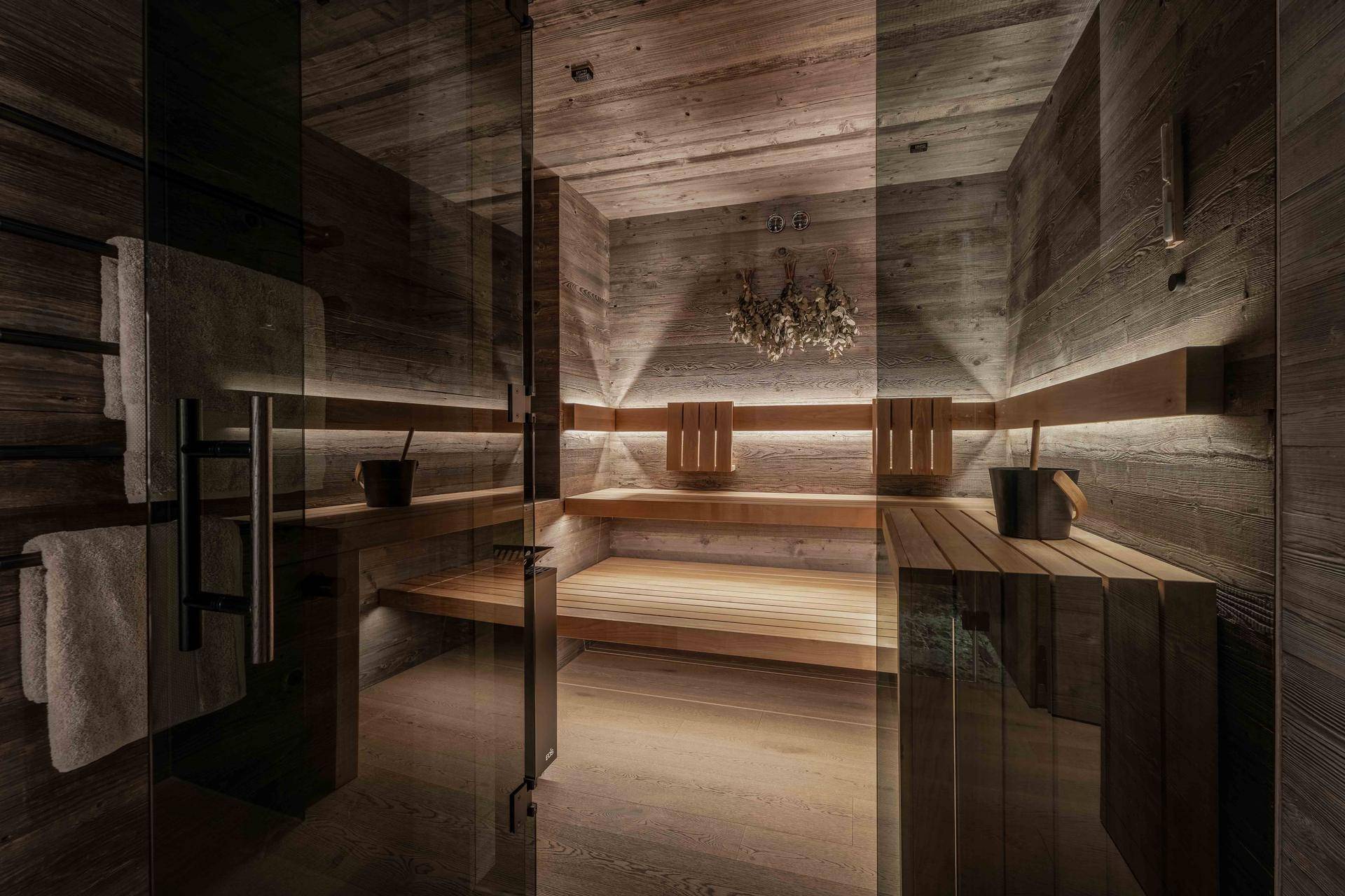 Moderne Sauna mit Holzwänden, Bänken und indirekter Beleuchtung für entspannende Momente.